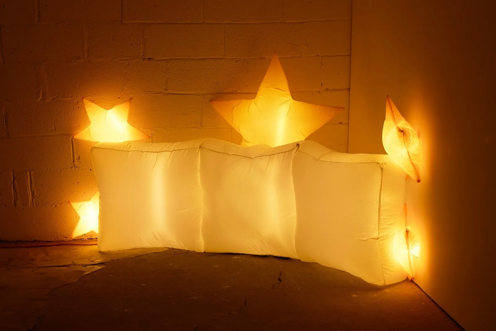 Inflatable pillow-shaped balloons and illuminated stars, sculptures installed at the corner of a gallery, jacob jackmauh every occasion 2025, resewn polyester inflatable decoration, jacob jackmauh admissions at parent company, solo exhibition nyc.