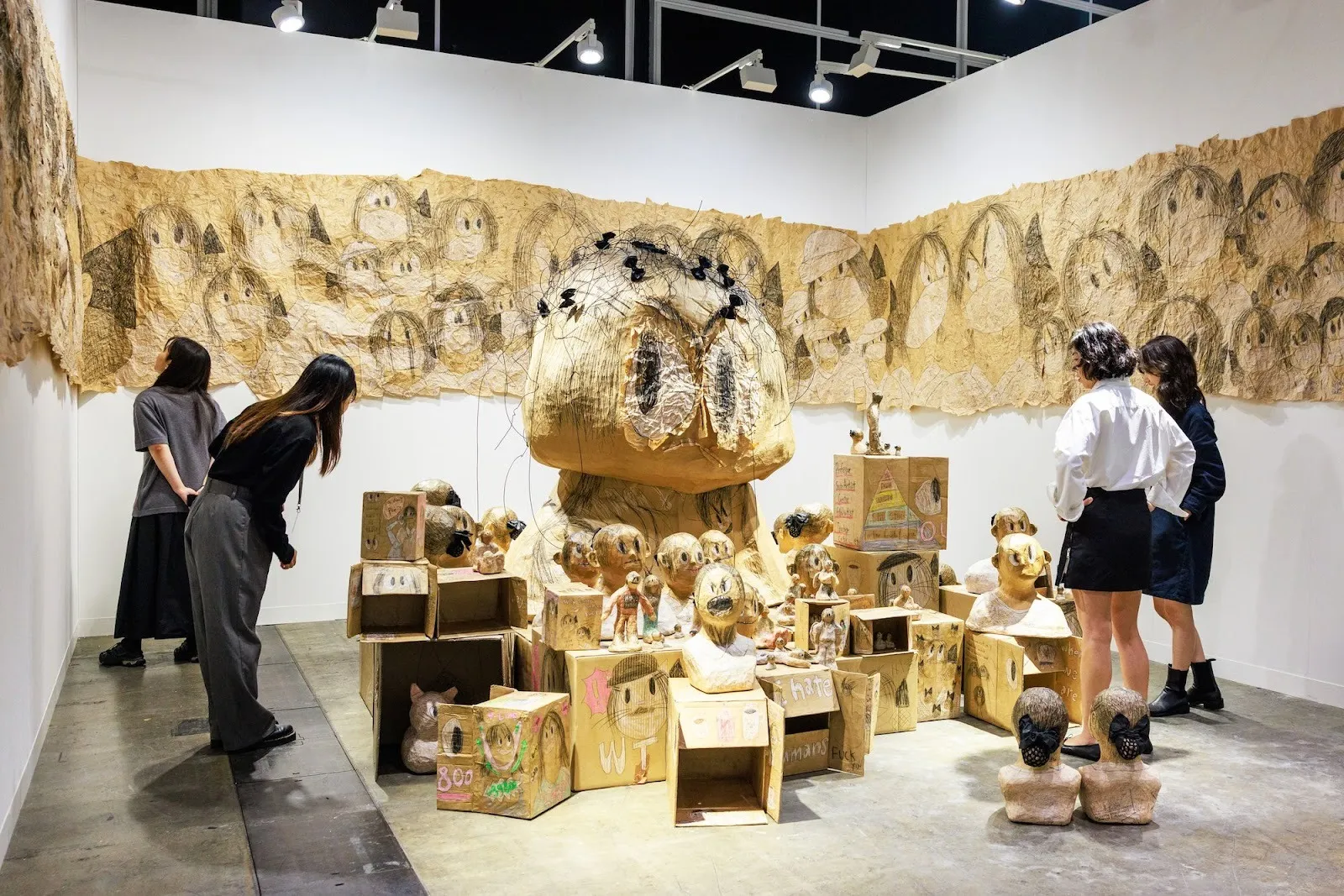 Art basel hong kong fair booth with knitted yellowish brown strips with human head drawing, woodblock installation at the center, shin min p21.
