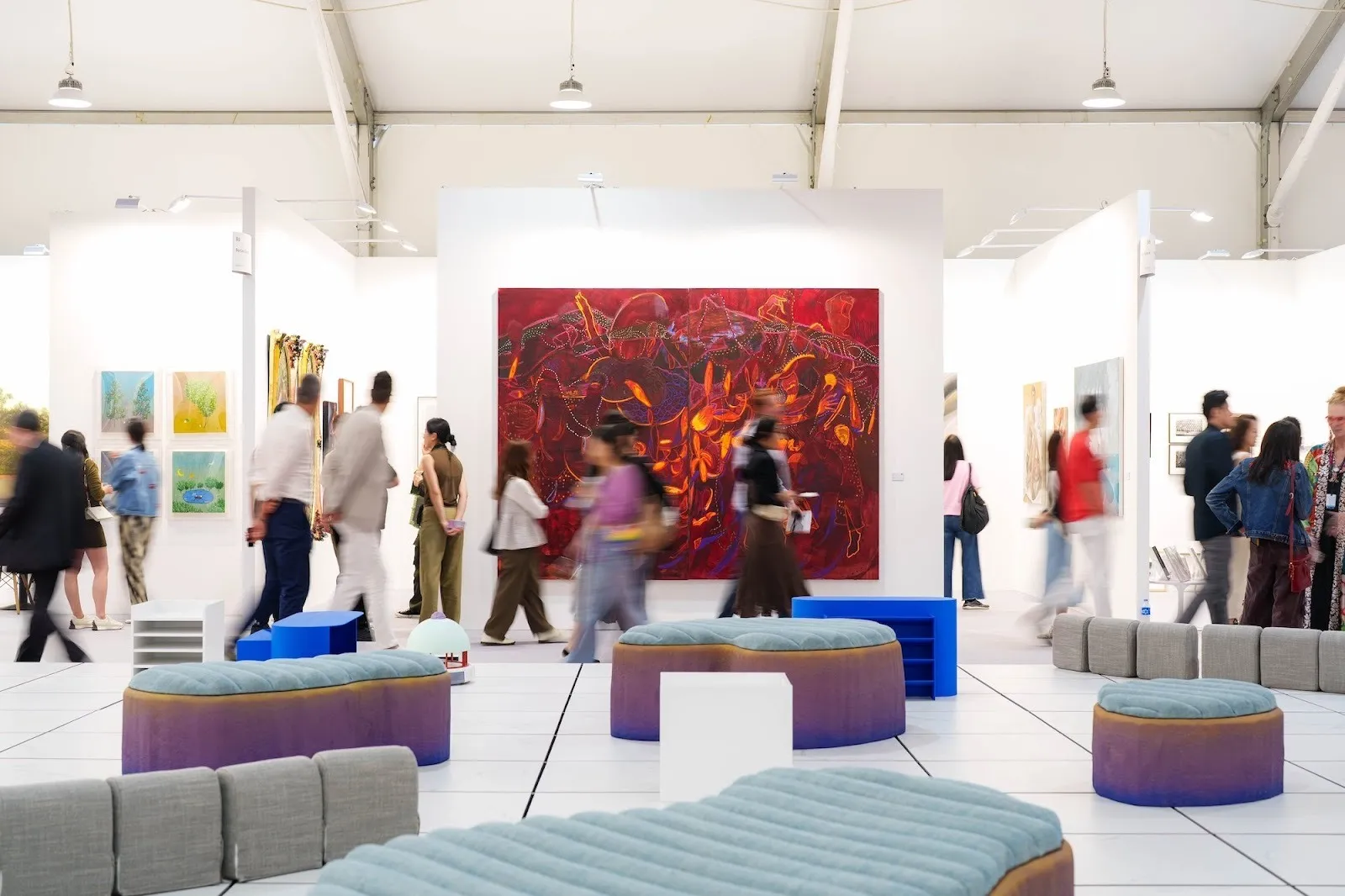 Art central 2025, hong hong art fair, booths with paintings installed and couches in the middle of the spaces, humans are walking past the exhibition spaces.