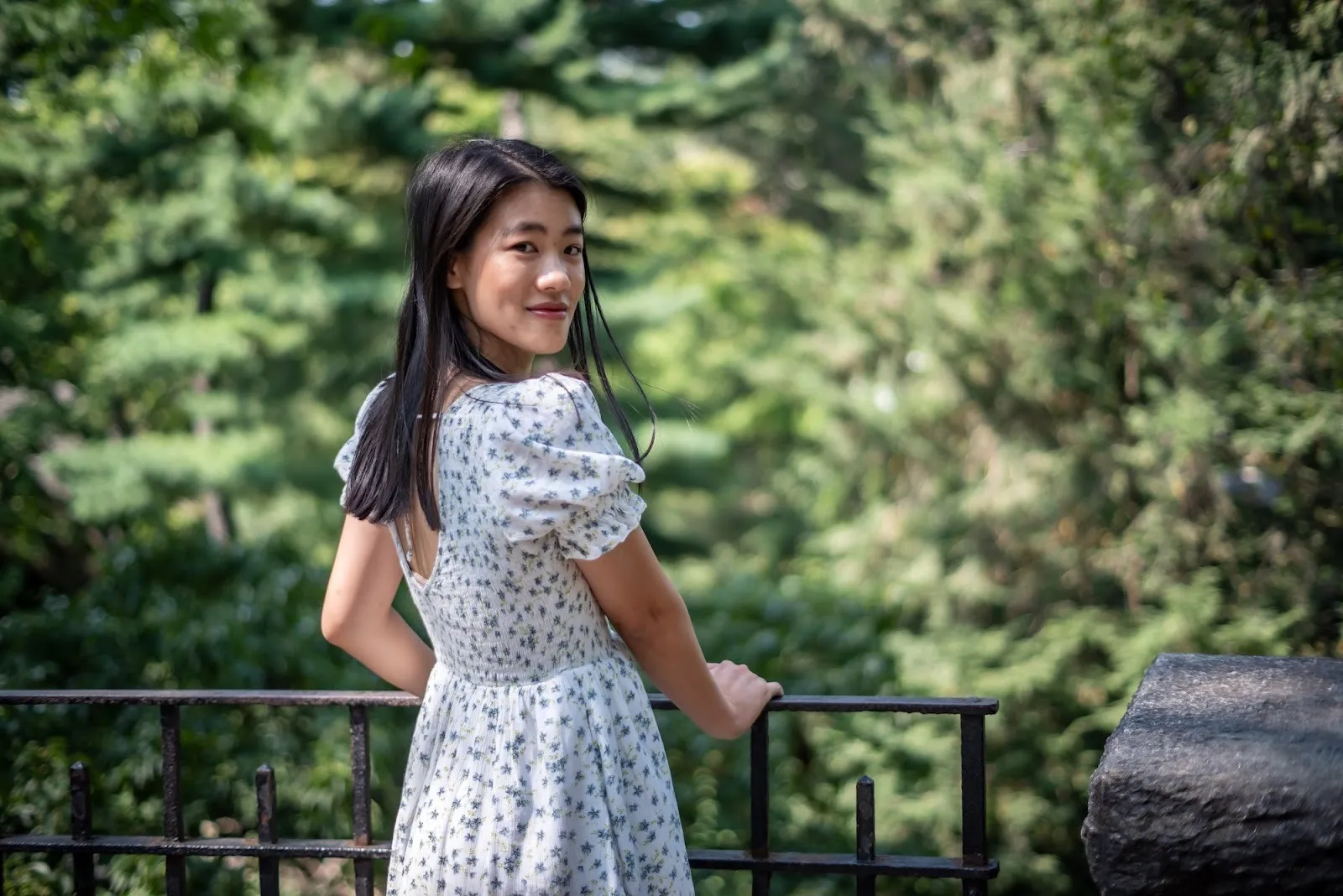 Actor Rebecca Ho wearing floral pale blue printed dress turning around to make eye contact with the audience in front of a park.
