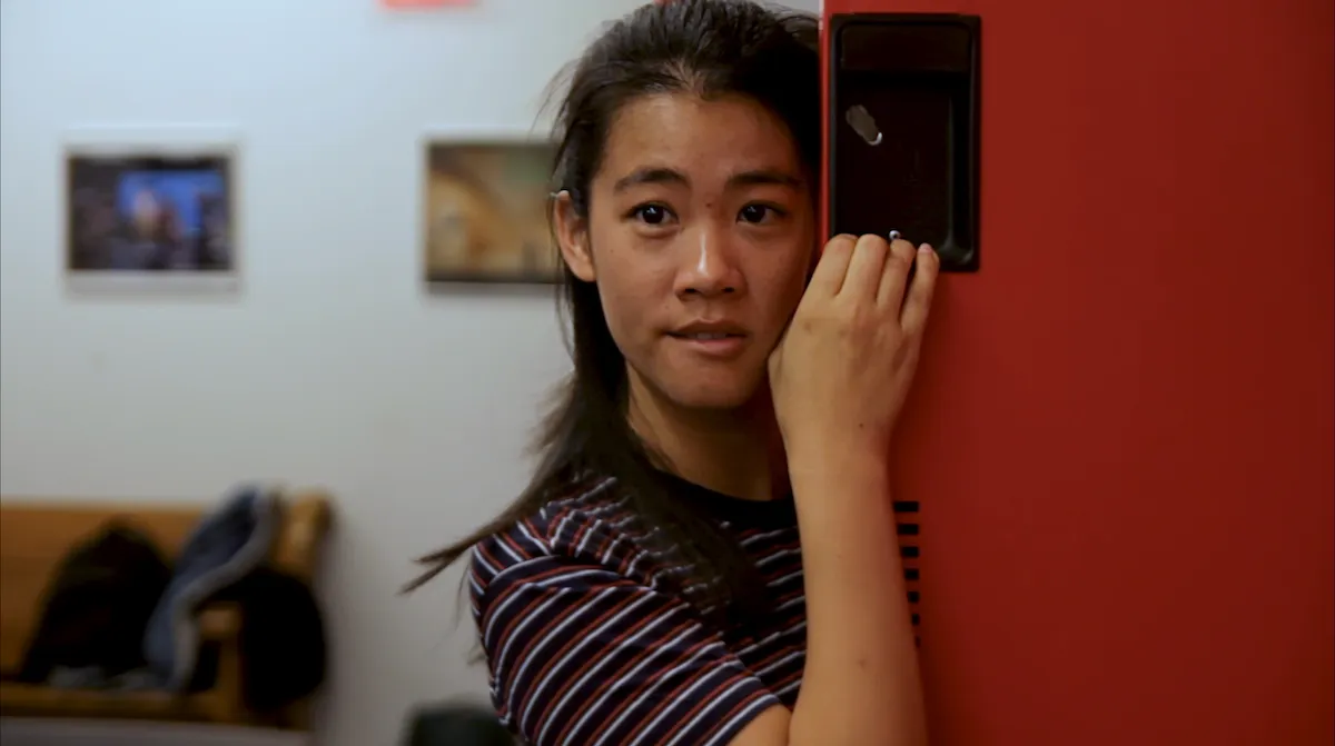Still of Rebecca Ho in the film High School Heartbreak, actor with dark hair wearing striped t-shirt half leaning against red door.