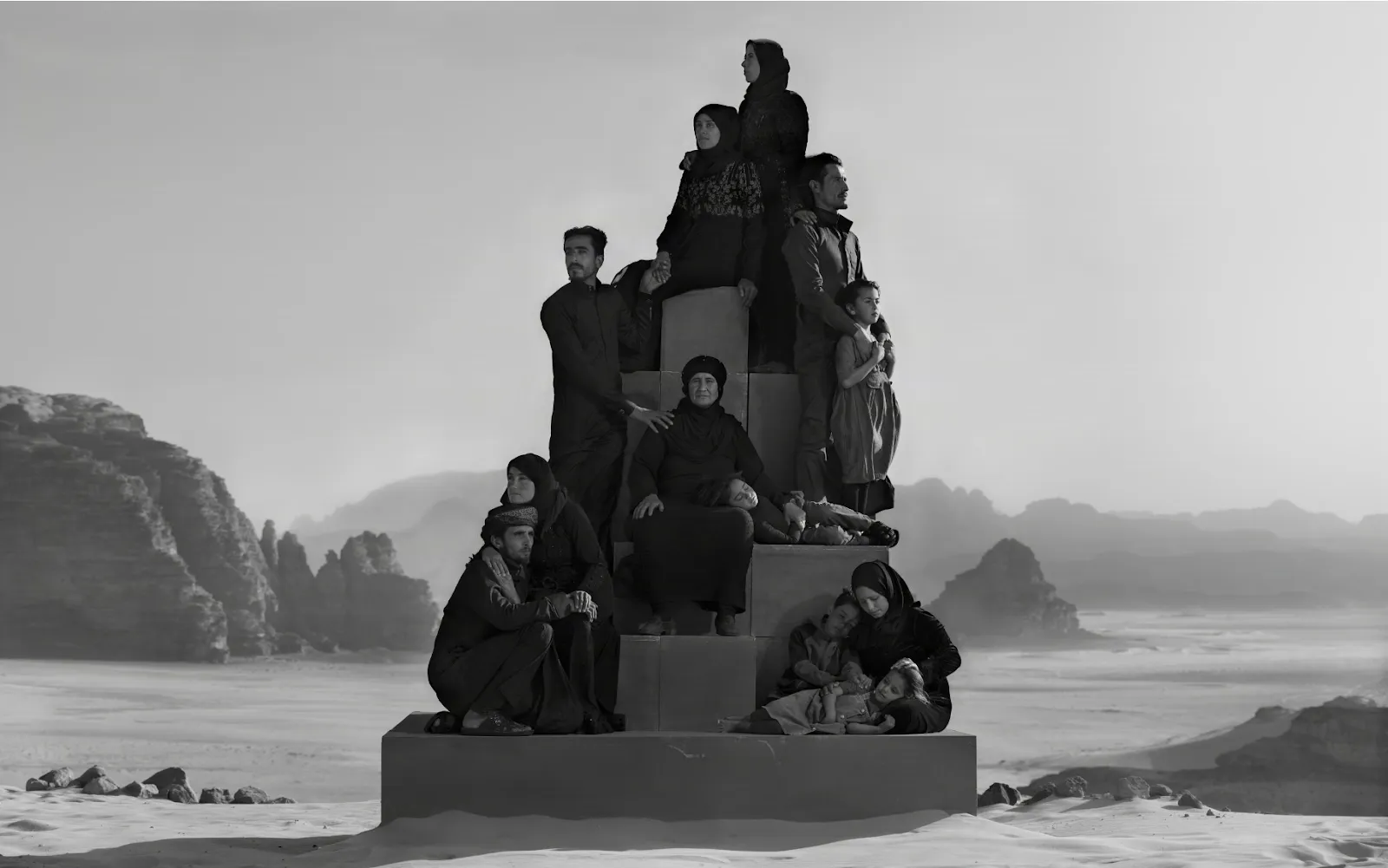 Nick brandt photograph of syrian refygee families in jordan, standing atop pedestal in the middle of desert landscape.