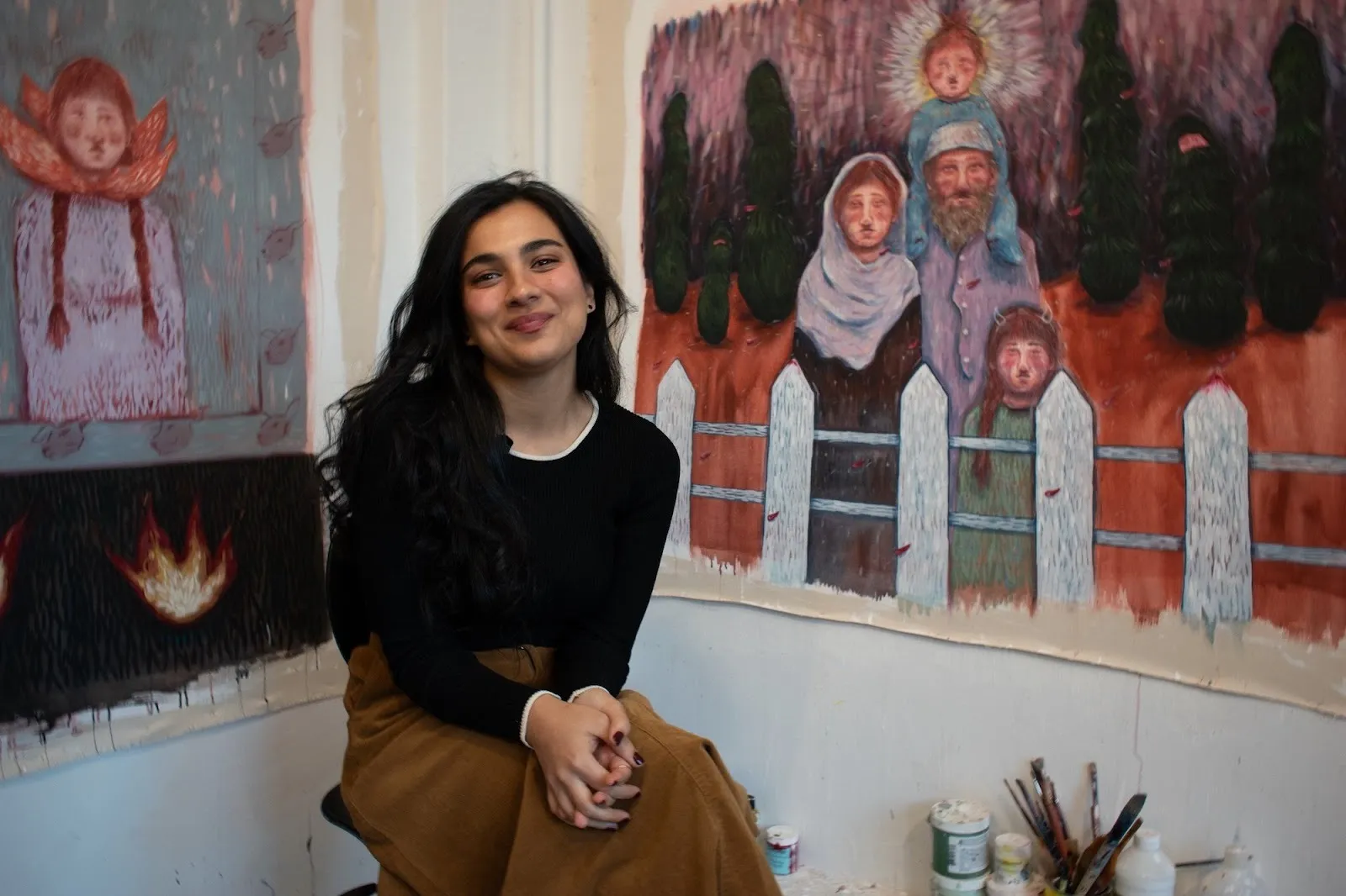 Photo of artist Noormah Jamal smiling in front of her paintings in her studio.