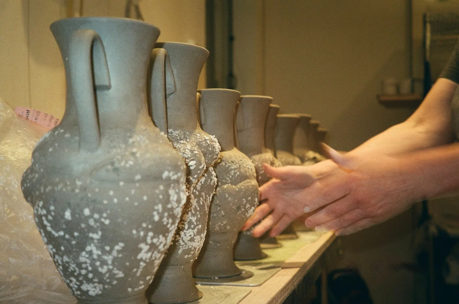 Photo of hands in motion, reaching to a row of unfinished clay amphorae.