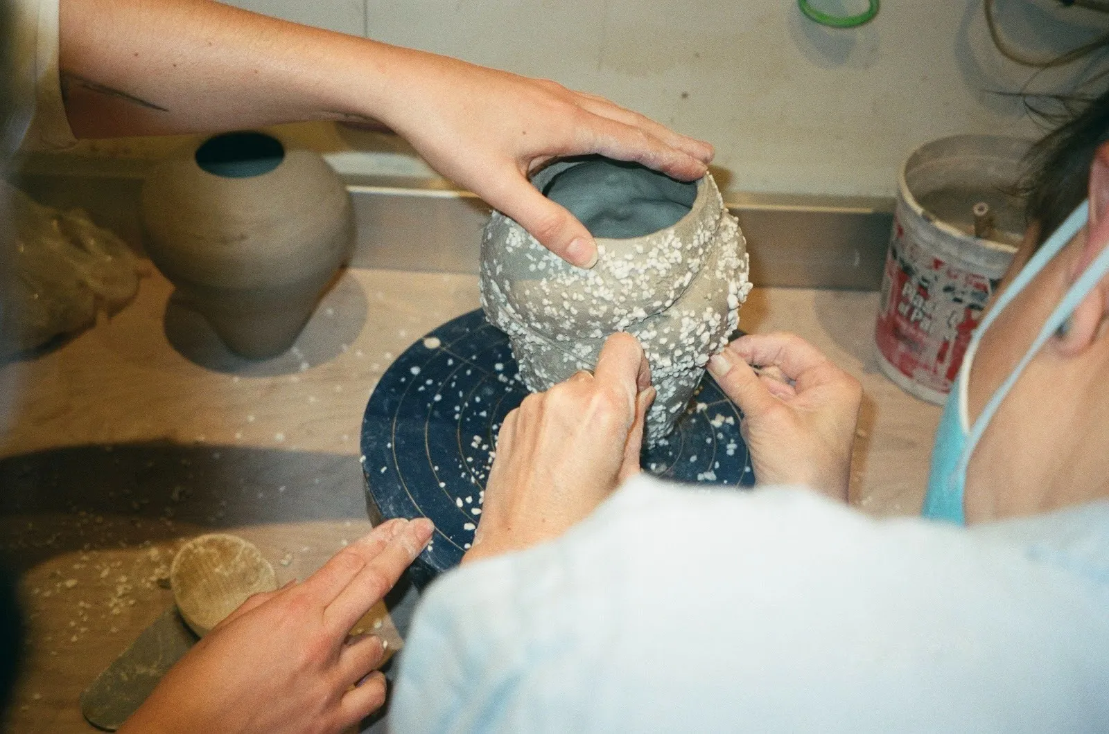 Photo of two people handling a clay form with irregular white spots. One holds the clay form, while the other tightens a wire around it.