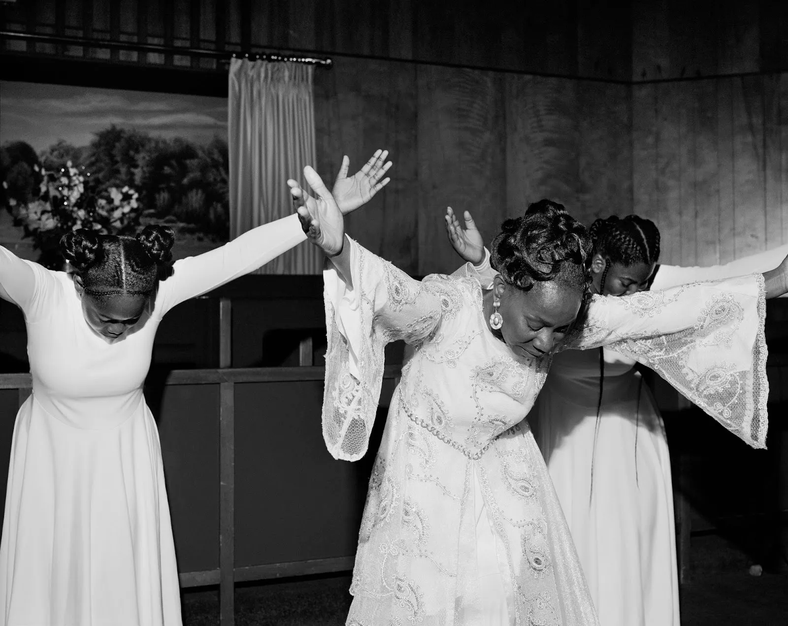 Black and white photograph of Praise Dancers wearing dresses and holding arms up while bending torso over, rahim fortune texas documentary photography from the series hardtack, reflections at howard greenberg gallery.