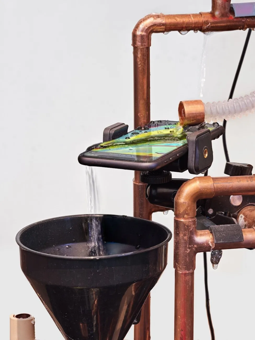 Copper pipe structure leaking water supports a touchscreen phone over a filter which catches the water.
