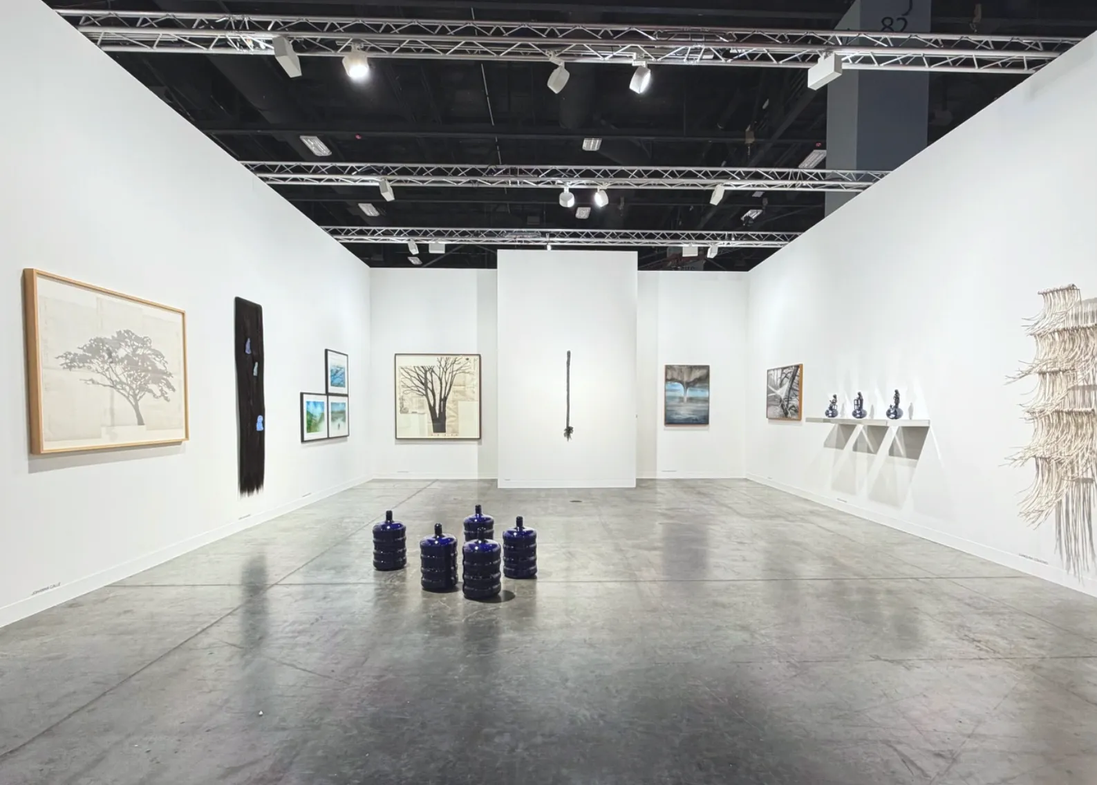 Minimal booth with framed landscape-style works on the walls and a cluster of dark blue ceramic vessels on the floor.