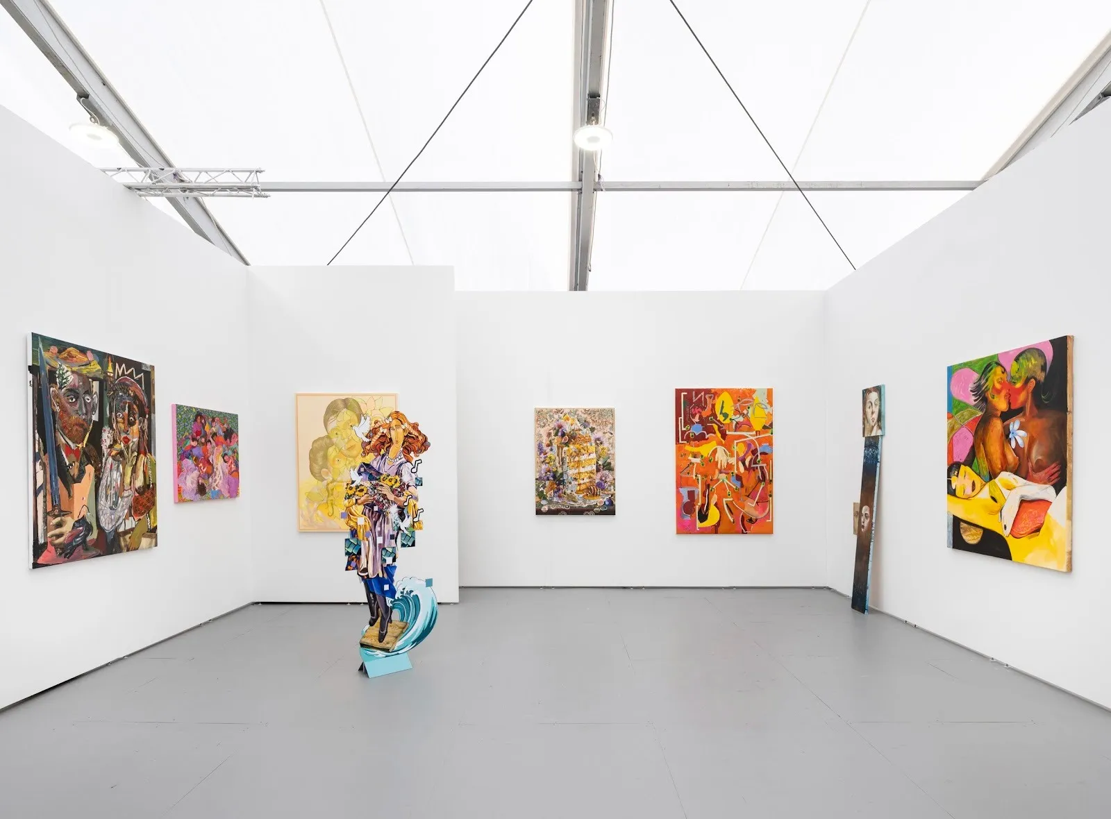 Booth displaying colorful figurative paintings and a freestanding cutout sculpture of a woman in the center.