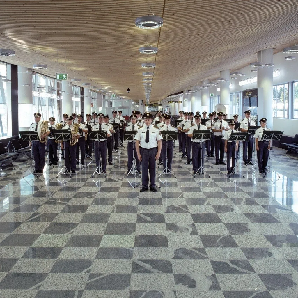 Guards in uniform standing in the hallway was music notes in front of them playing instruments, political theater tourists welcome I Feel Love, jasmina cibic artwork.