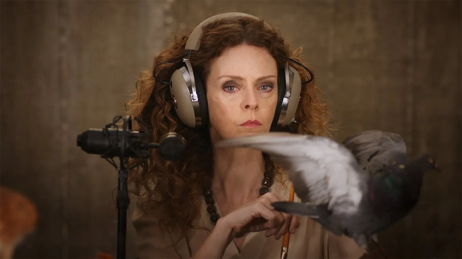 Woman with curly hair in front of a microphone wearing headphones looking into the camera seriously, flying pigeon in front of her, jasmina cibic artwork.