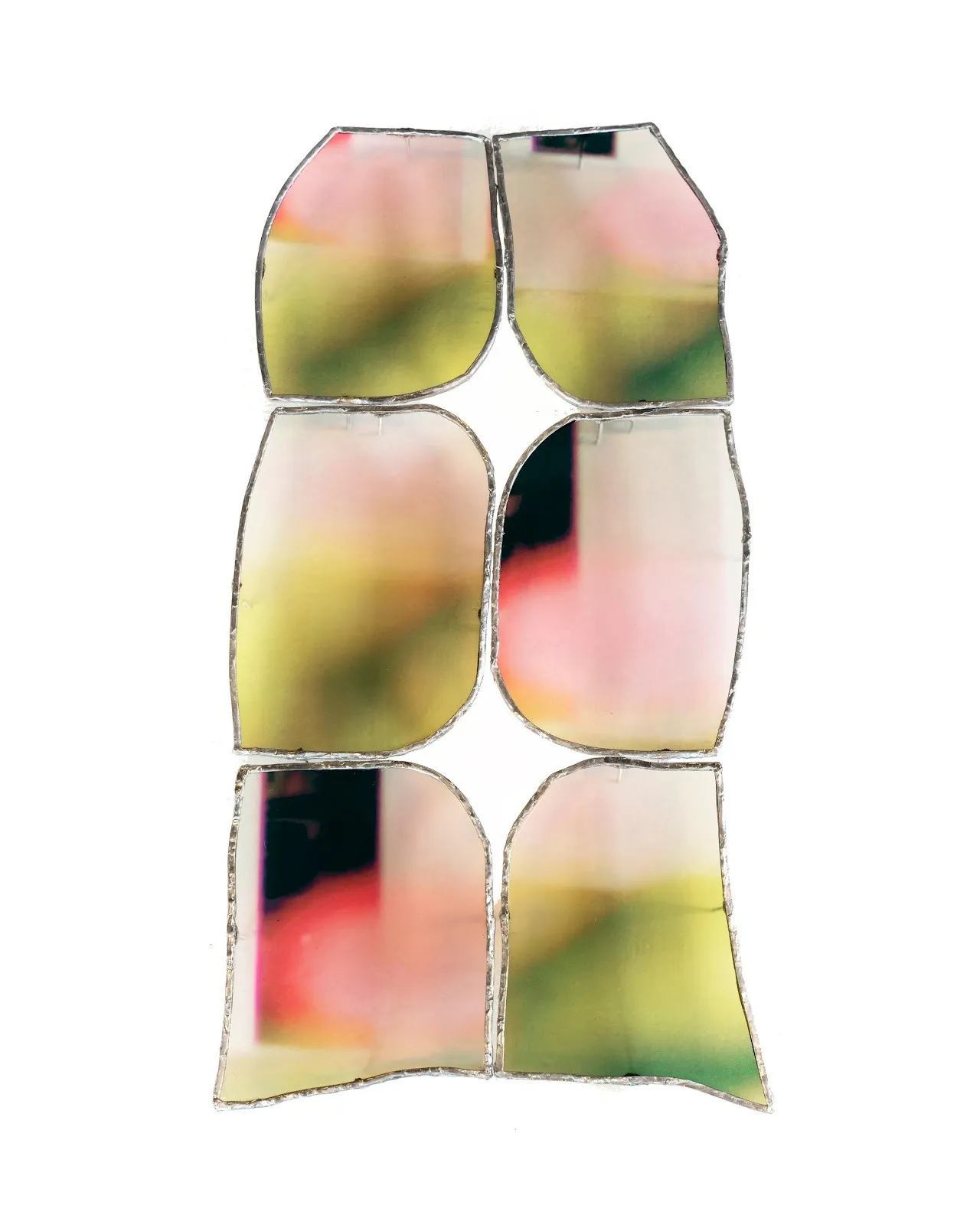 A grid of six loosely-fitted glass tiles with silver edges come together in vertical alignment. Each pane of stained glass has soft variations in shade, ranging from pink to black to green and yellow.