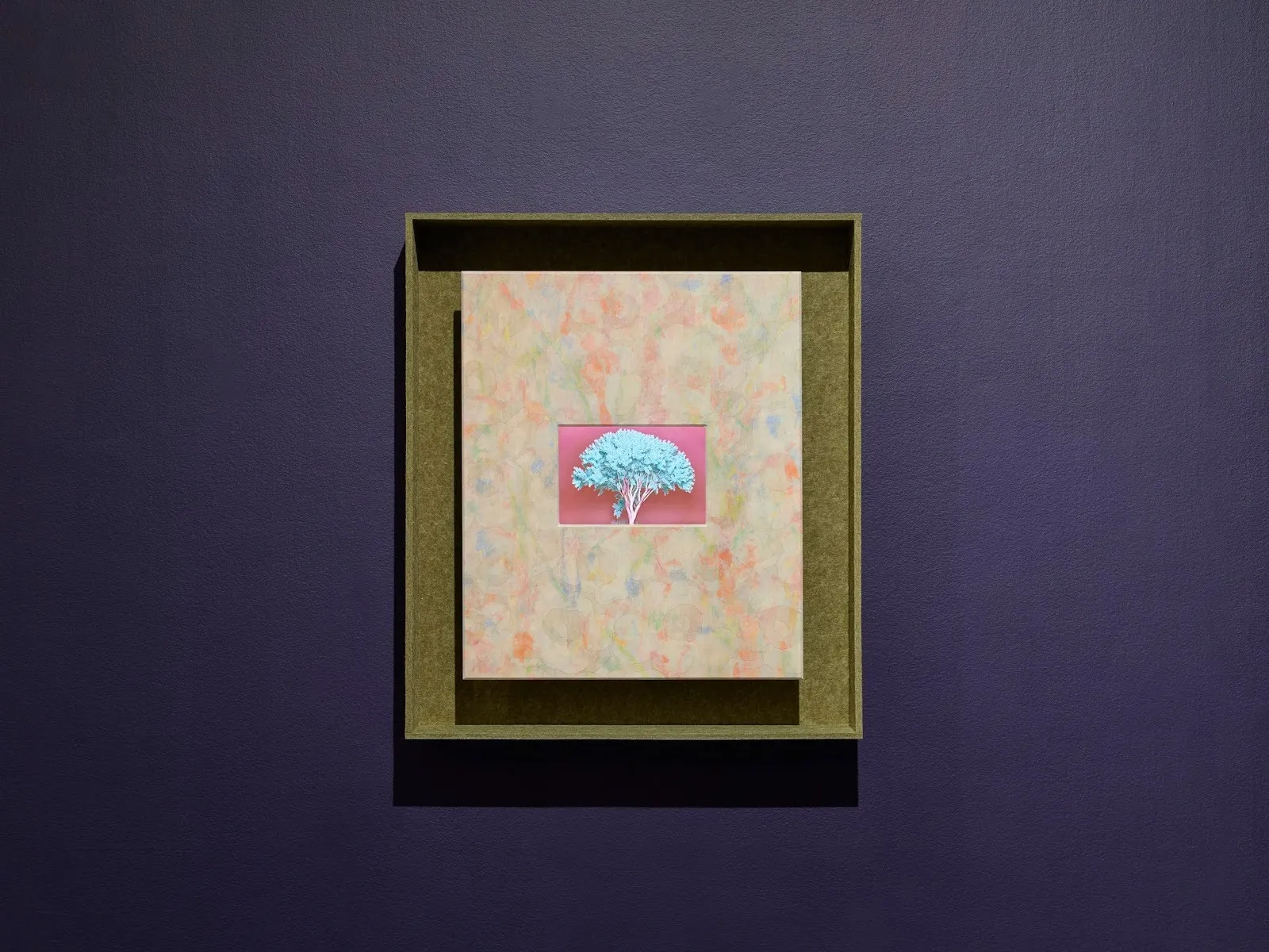 A navy wall with a small/medium-sized, green-framed painting. The painting is rendered in multiple soft colors which frame a small center of a cyan-colored tree against a pink background.