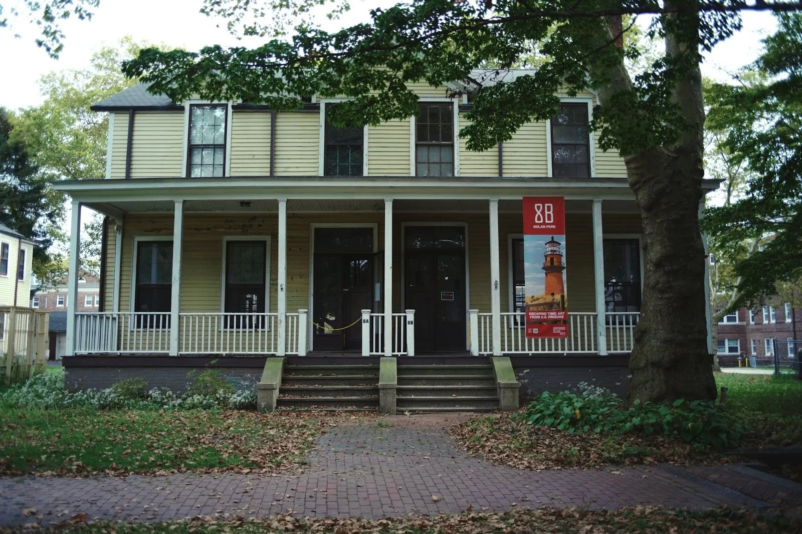 A two-storied house with a porch and double stairs features a slim banner on its right.