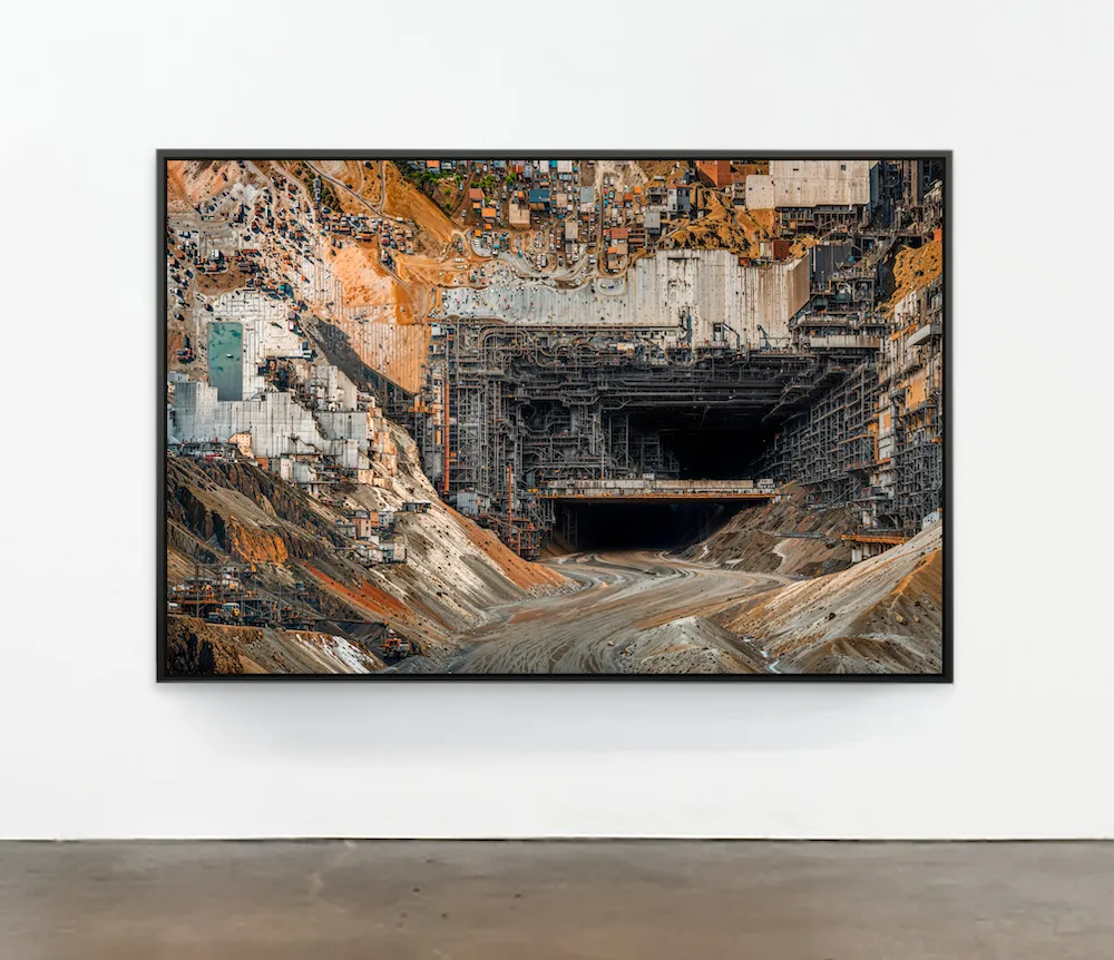 A white gallery wall features a large, framed painting of a surreal, detailed mix of an industrial aerial view and a dirt landscape.