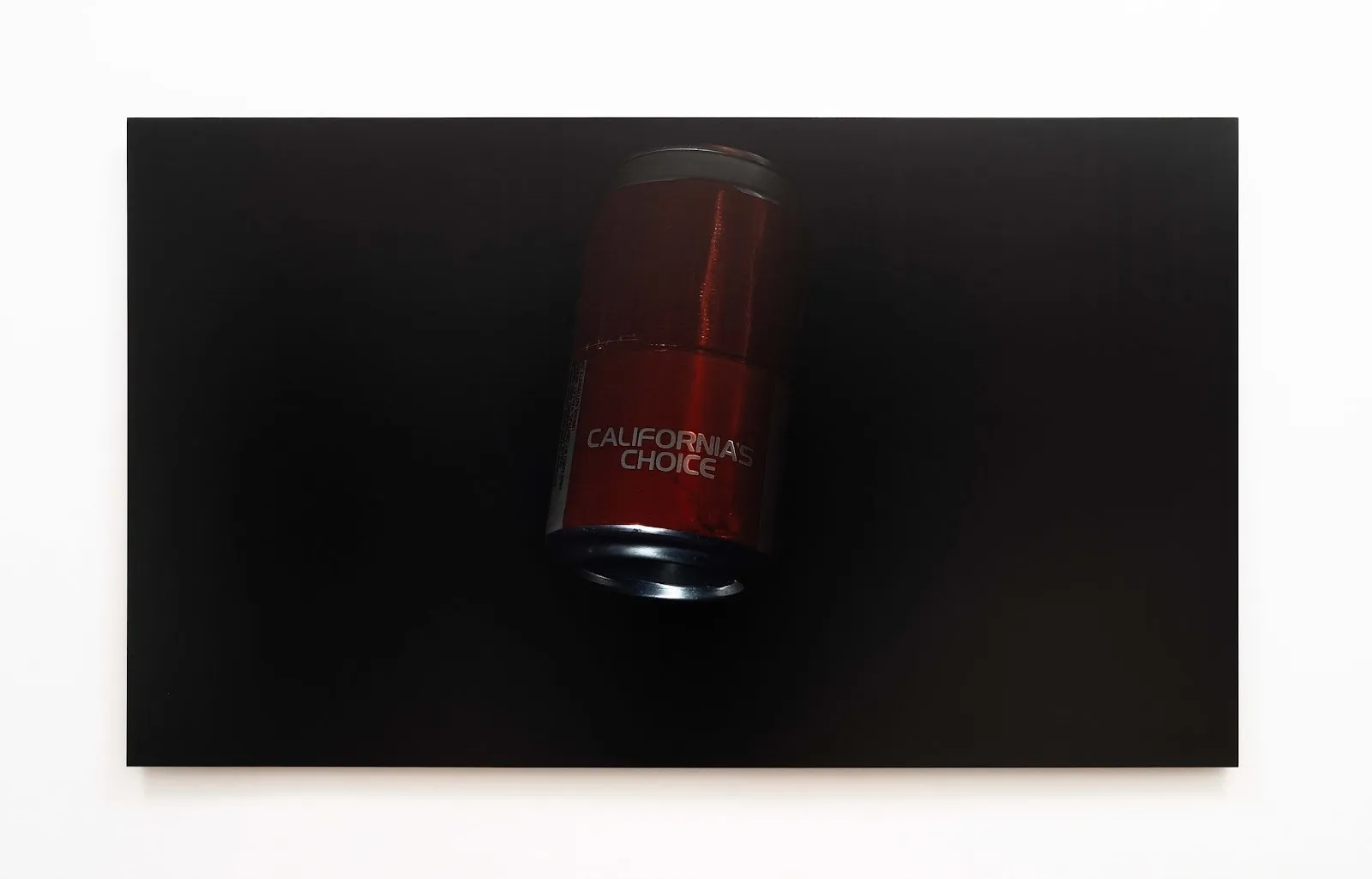 A white wall features a large horizontal work. The work features a dimly lit, red soda can with the words "CALIFORNIA'S CHOICE" against a dark background.