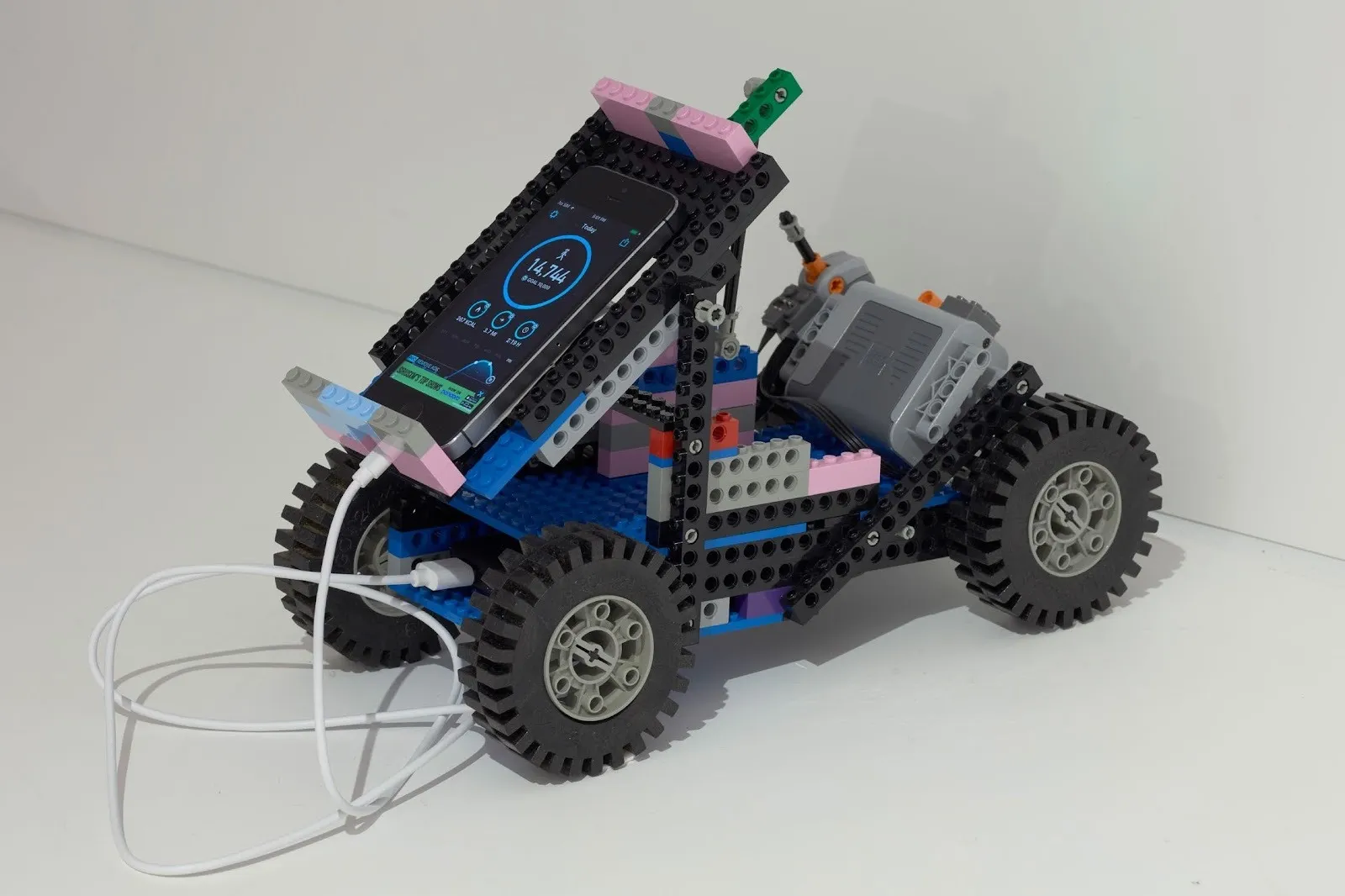 A rudimentary car-like object made from lego holds a phone plugged into the device. The phone screen features health stats.