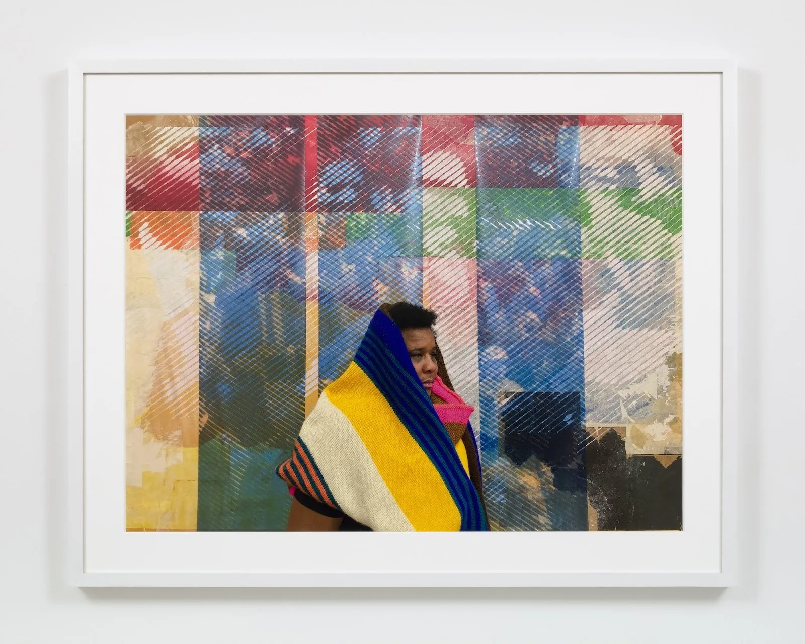 A person wrapped in colorful blankets look to the right of an artwork, screen prints with colorful stripes including blue red and green on top of archival photographs, artwork by tomashi jackson.