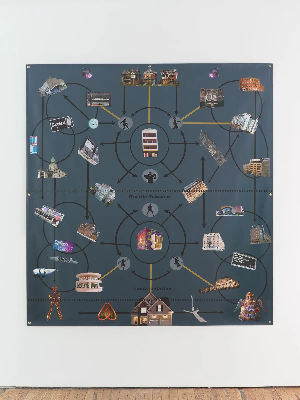 A 2D work mounted to a white wall is comprised of A grey background with cutout images of various buildings, signs, and objects connected by lines and black arrows, creating a diagrammatic composition.