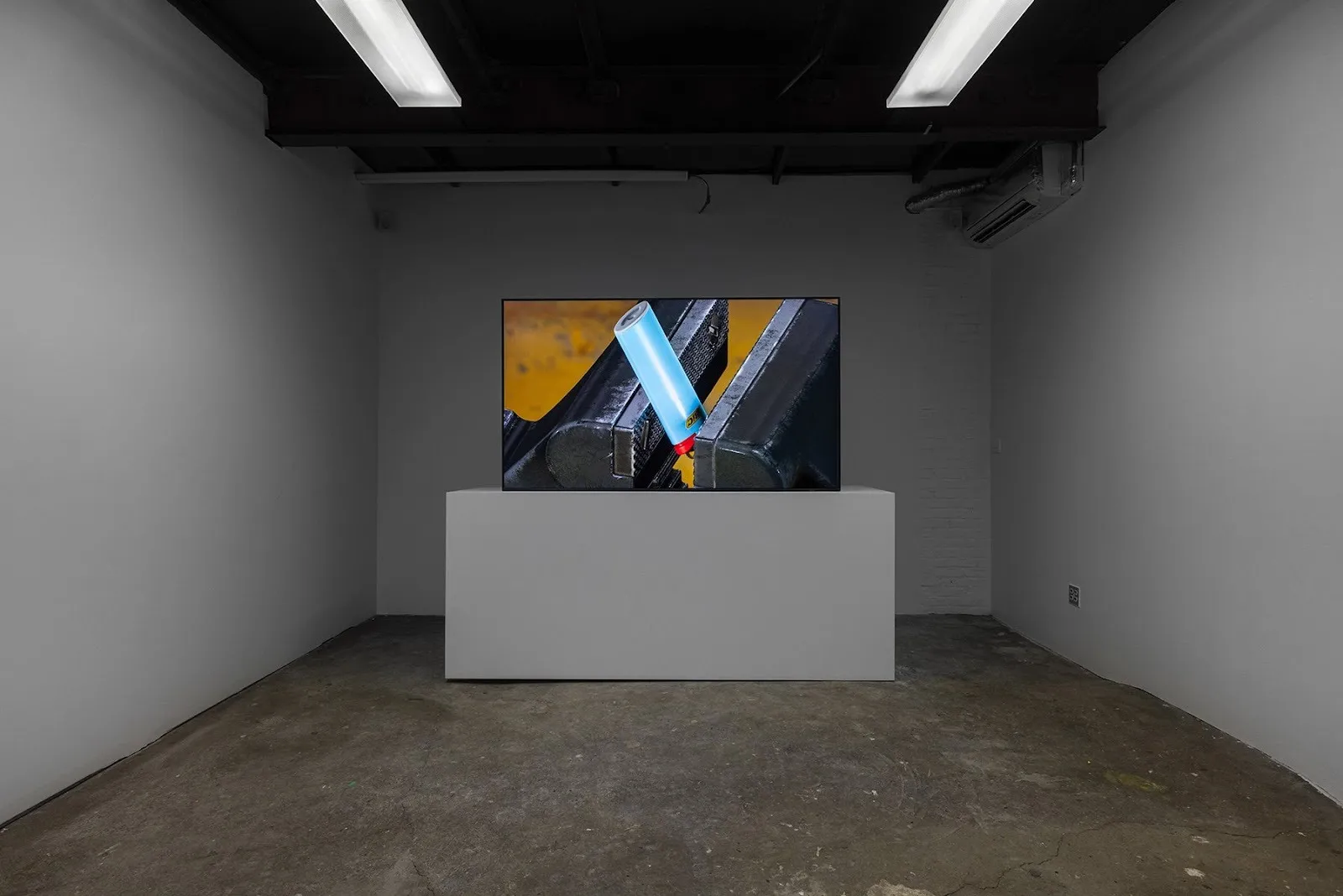 Grey gallery room with tv monitor screening a video of anvil burning in flame, Gregory Kalliche, Anvil (2025). 4K video with sound, 9-channel lighting program, DMX controllers, lighting interface.