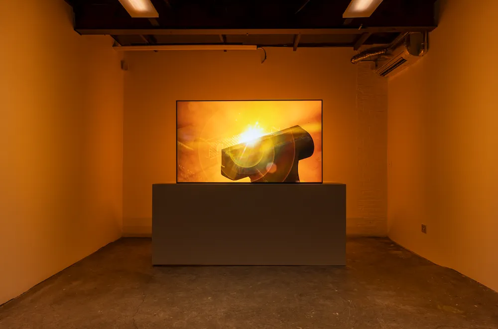 Room lit in bright orange with tv monitor screening a video of anvil burning in flame, Gregory Kalliche, Anvil (2025). 4K video with sound, 9-channel lighting program, DMX controllers, lighting interface.