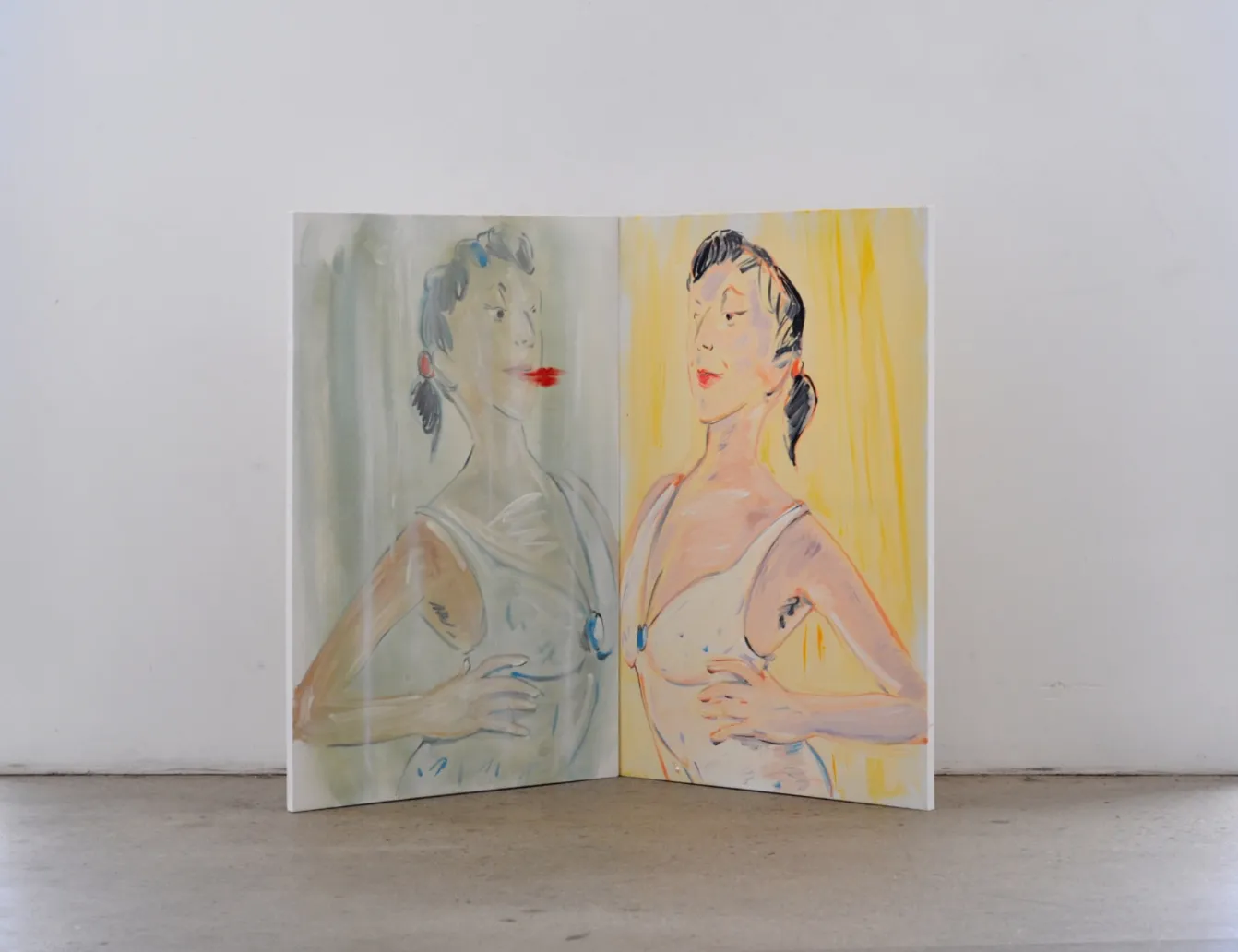 A diptych stands on the floor, folded like a half-open book. The figures stare at each other, the left image seeming like the mirror image of the right. The mirror image also has a bright read smear next to the lips, like a lipstick mark.