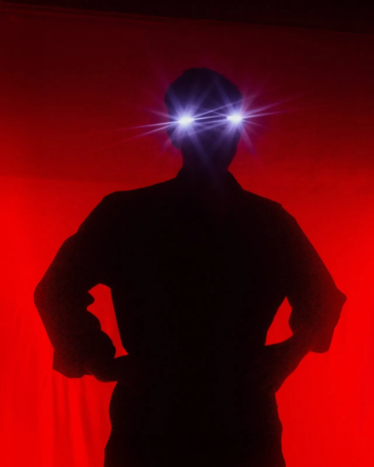 Silhouetted figure stands hands-on-hips against a glowing red backdrop, eyes emitting bright star-like beams of light.