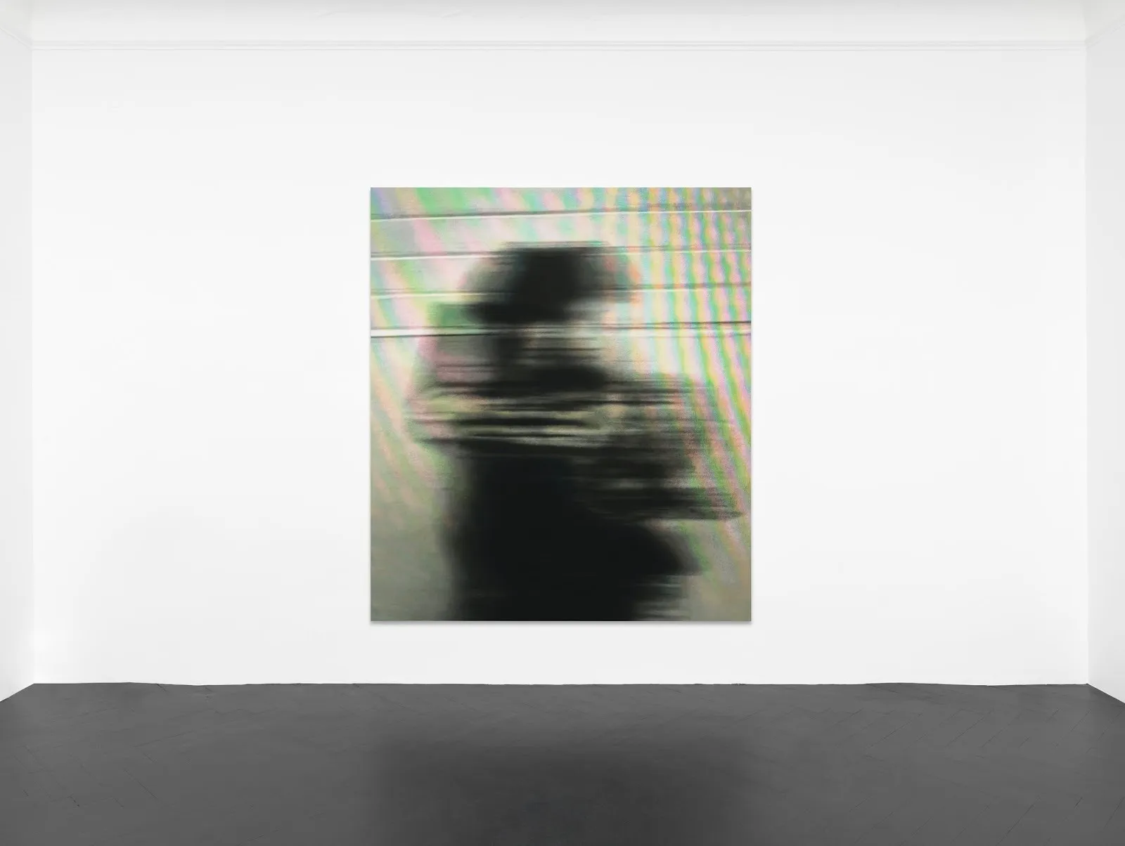 A single painting hangs central in a white gallery room with black floors. The paintings seems to depict a black and white blurred figure against a grey background, the whole work overlaid by a screen-like iridescent sheen.