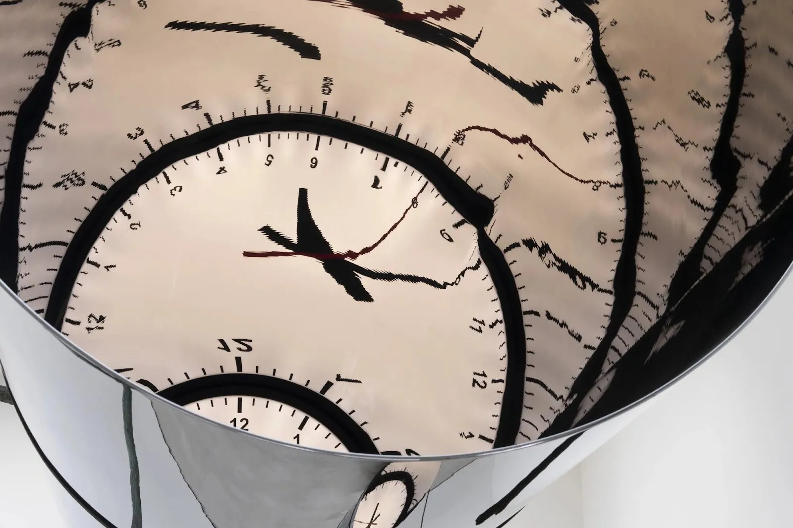 A chrome tube houses an illuminated analog clock face. The light from the clock creates warped reflections on the sides of the tube.