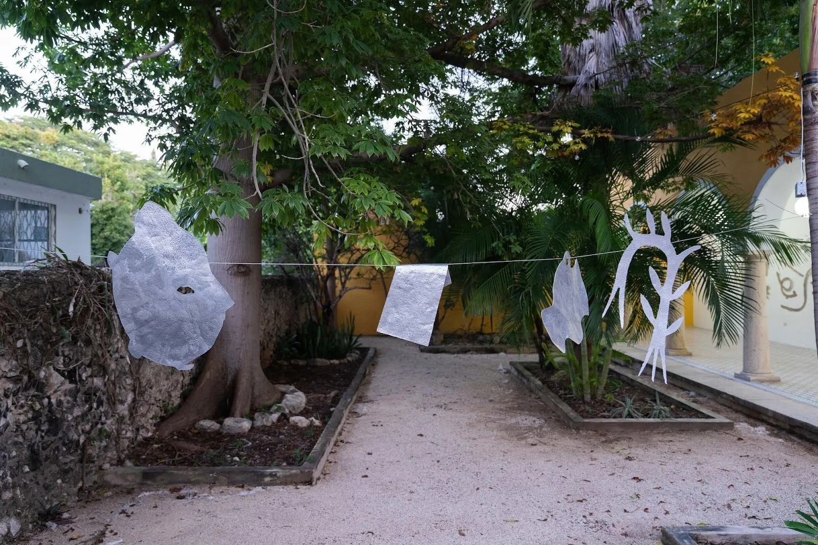 Thin silver metal cutouts in organic shapes hanging from a clothesline in a lush outdoor garden.