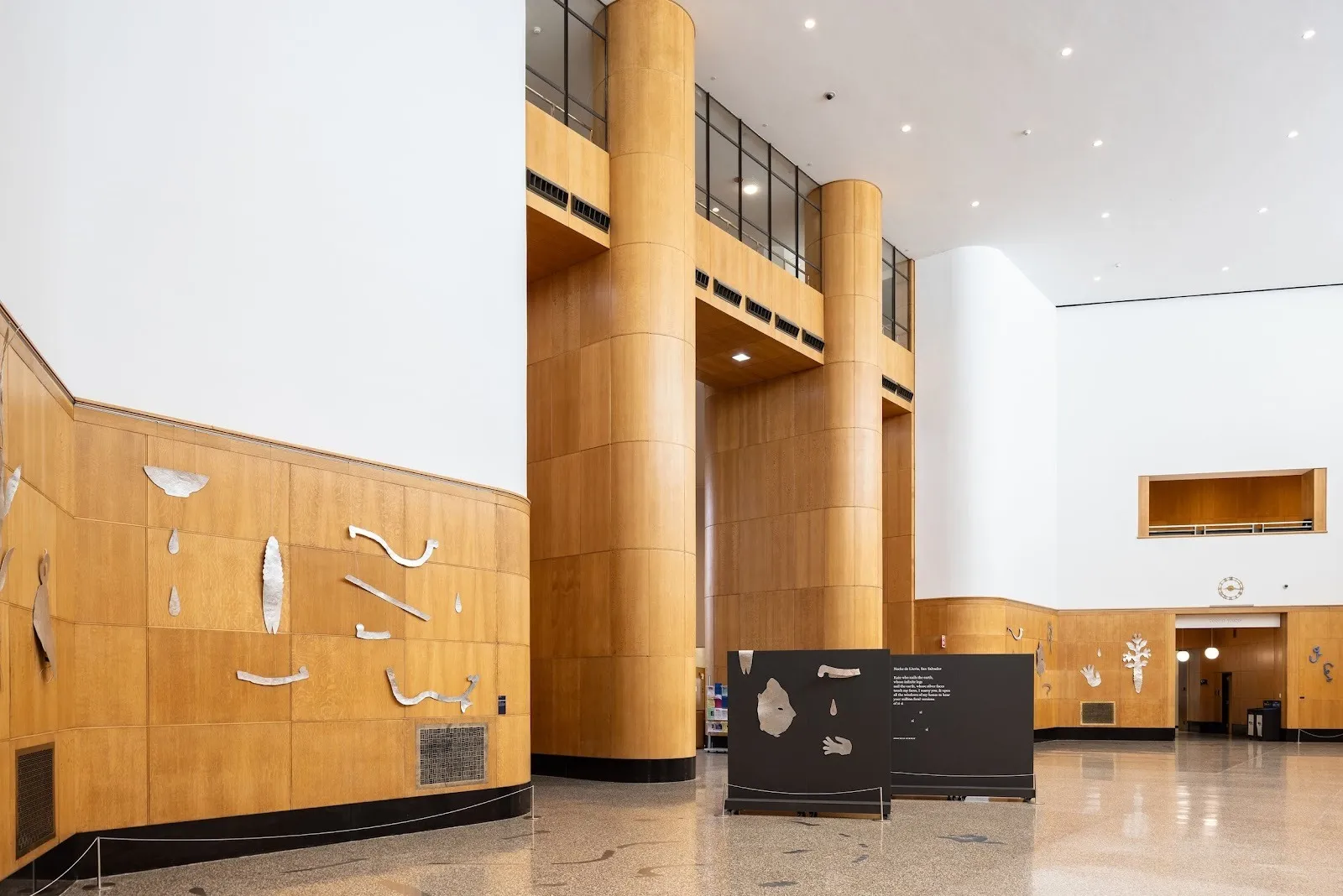 Large lobby installation with silver metal shapes mounted on warm wood paneling surrounding a tall atrium.