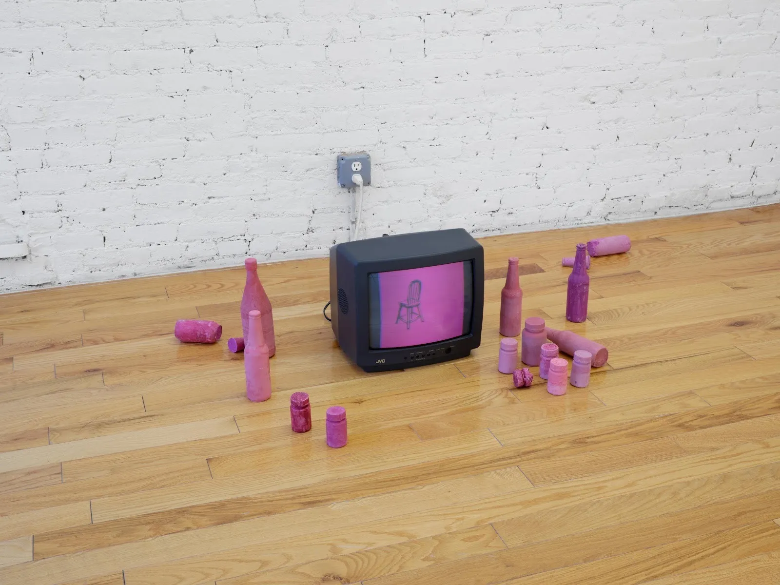 On a hardwood floor, an older TV displays a magenta-washed image of a wooden chair. Around the TV, magenta-painted bottles of various sizes litter about.