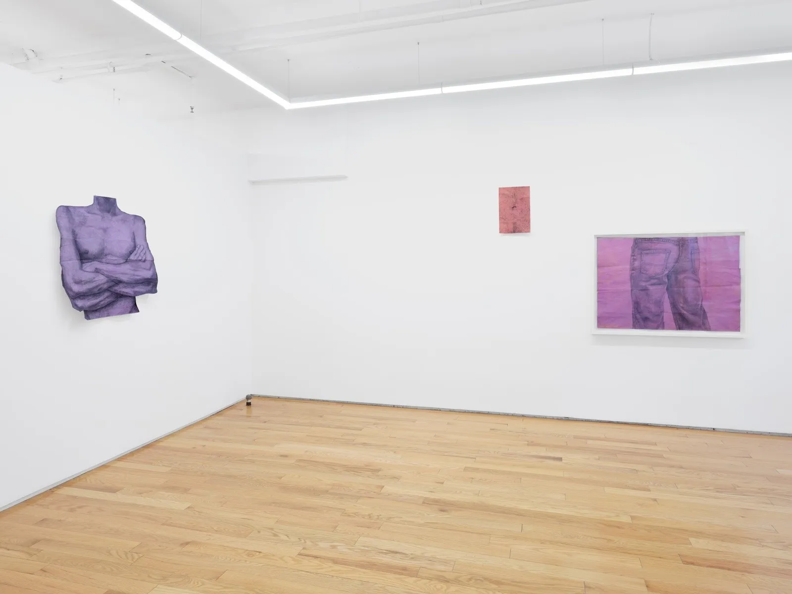 A white gallery room exhibits three works on paper. One is dye-cut to a headless torso with crossed arms, washed in purple. Another depicts a drawing of jean-clad legs from behind, washed in purple-pink. The other is a small, red work.