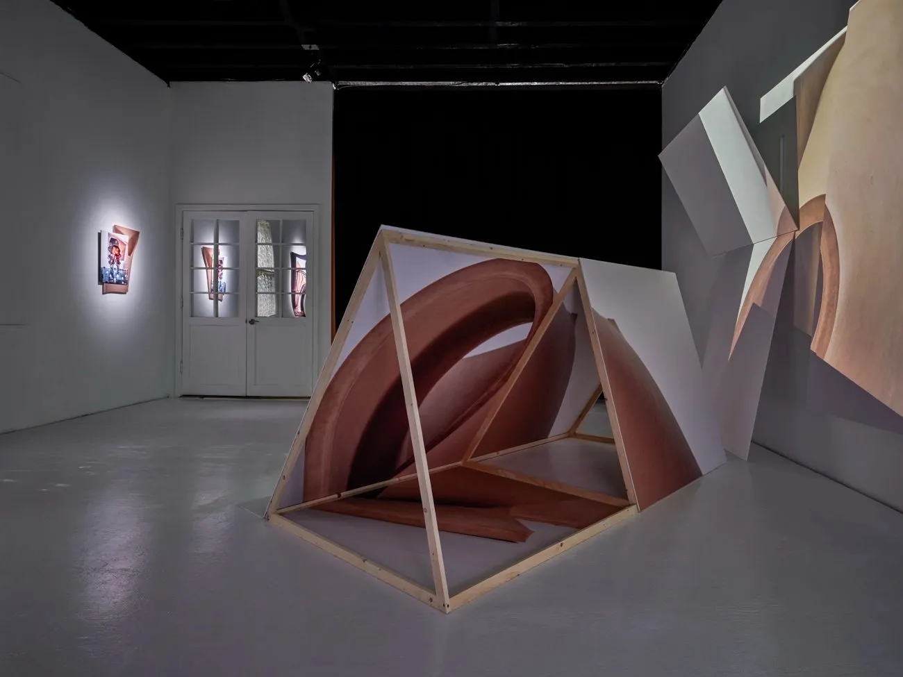 Gallery view featuring a large, triangular, wooden-framed structure covered in a photograph of a swirling, abstract form.