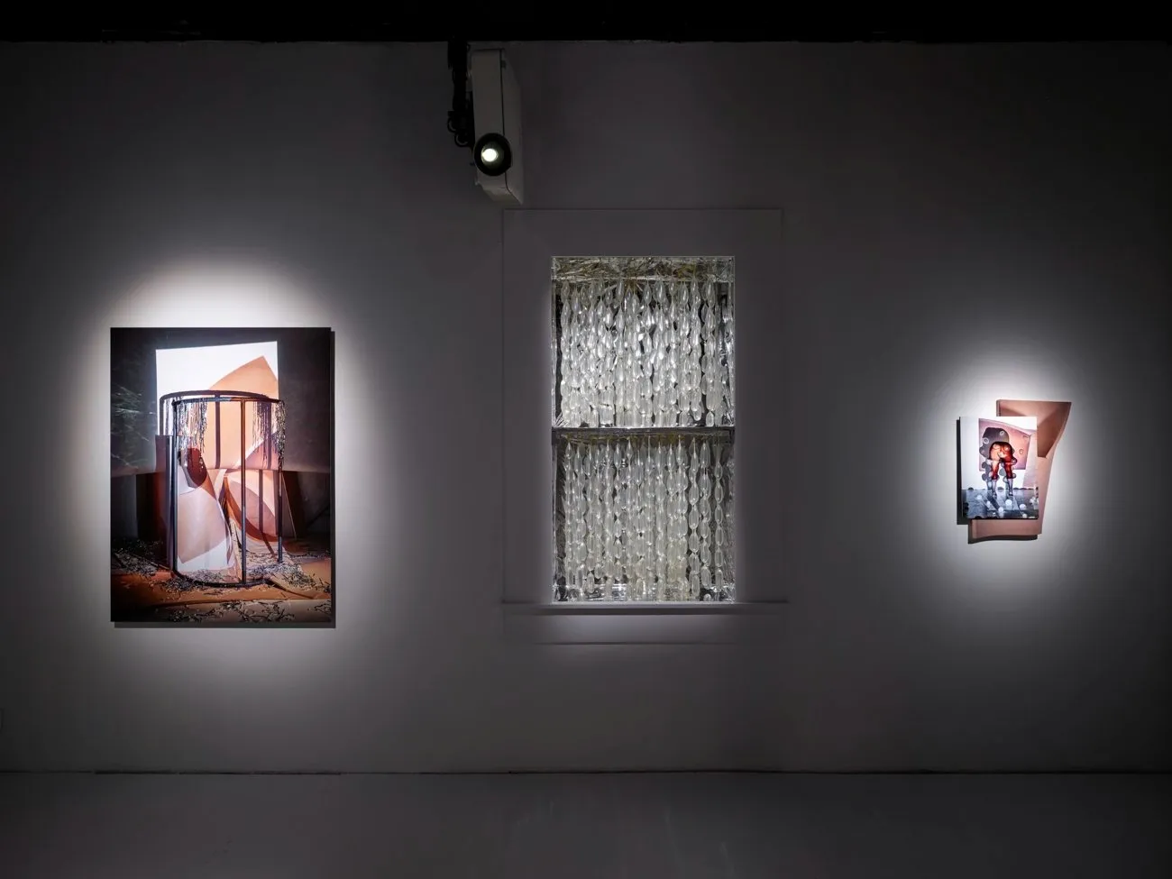 Three pieces of art displayed in a dimly lit gallery: a large photograph, a window with a glass bead curtain, and a smaller photograph.