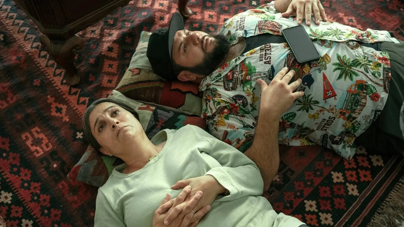 Two people lie on their backs on pillows and a rug. They stare at the ceiling.