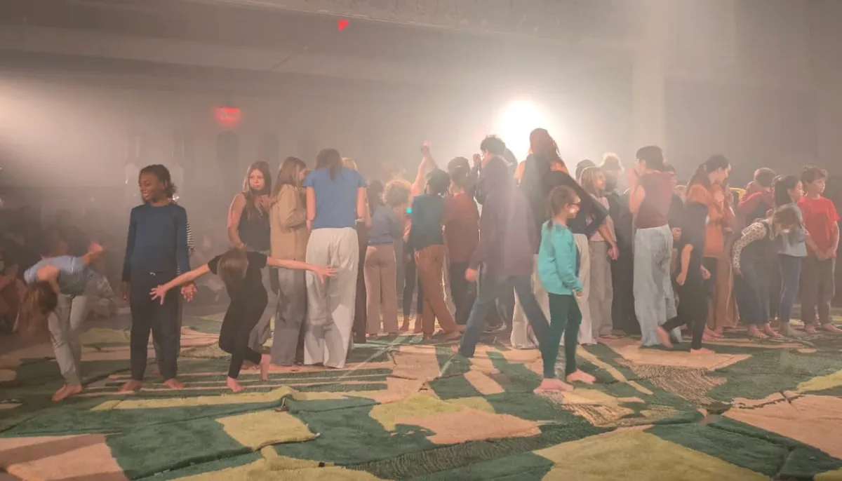 On a heavily pink-and-green blanketed floor, a crowd of children gather and move about the floor.