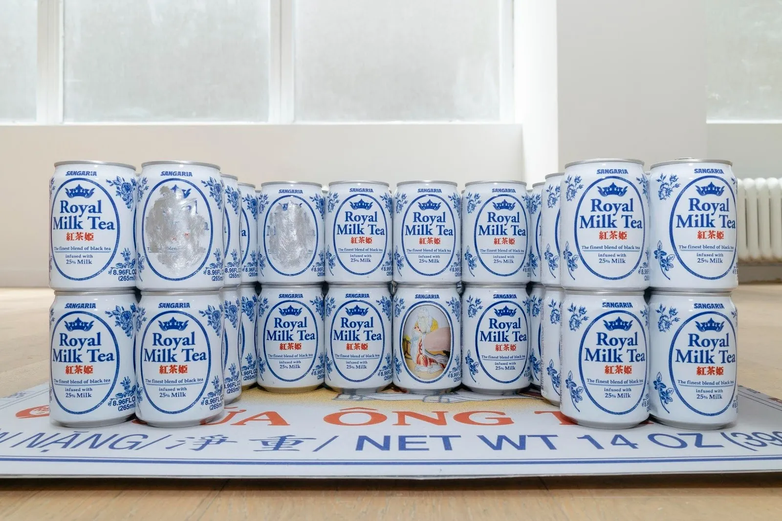 Configured stacks of Royal Milk Tea cans rest on a large printed image set on the floor of a gallery space.