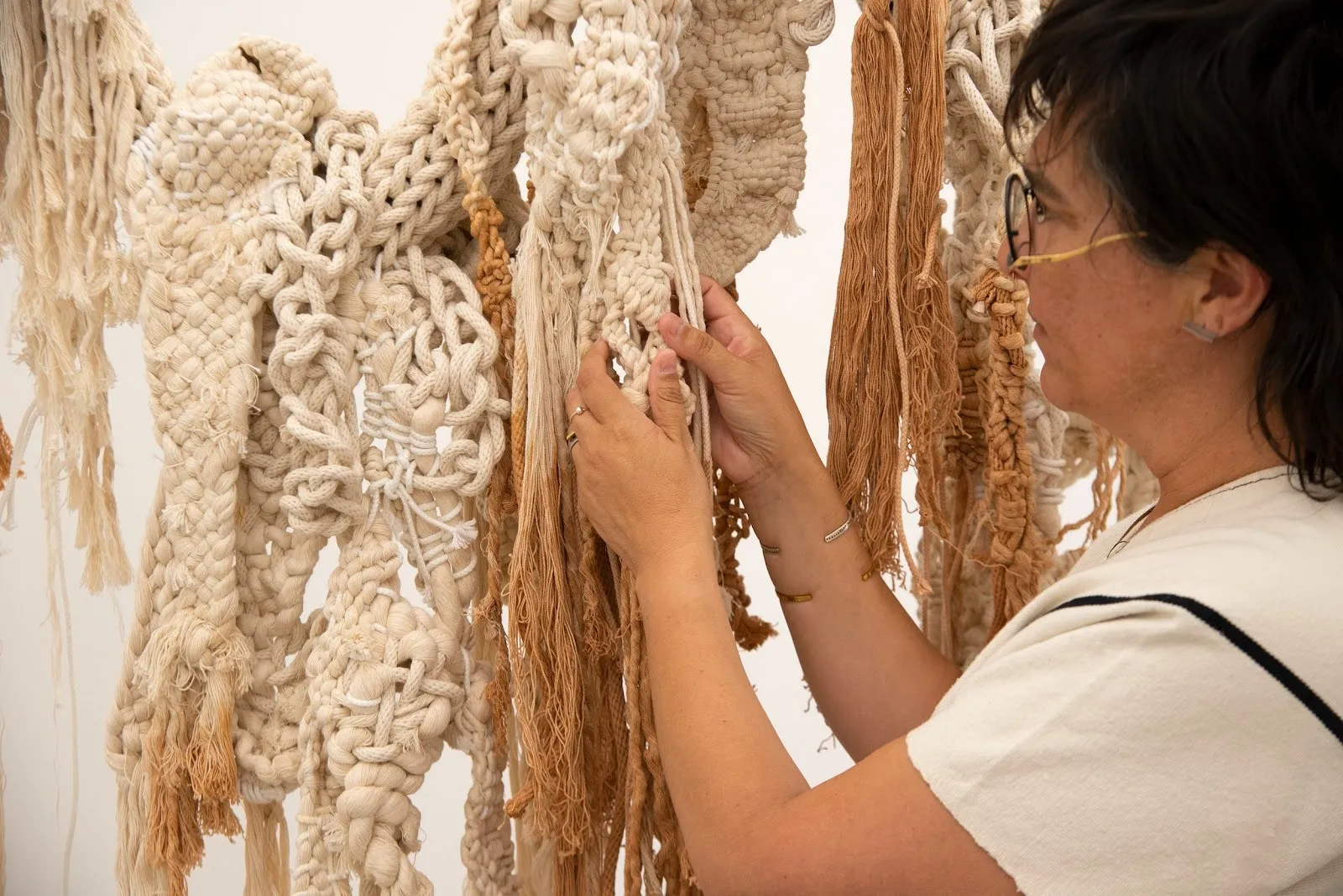 A person gently grasps braided ropes and fibers in tan and beige colors. The fibers are of different sizes and configurations.