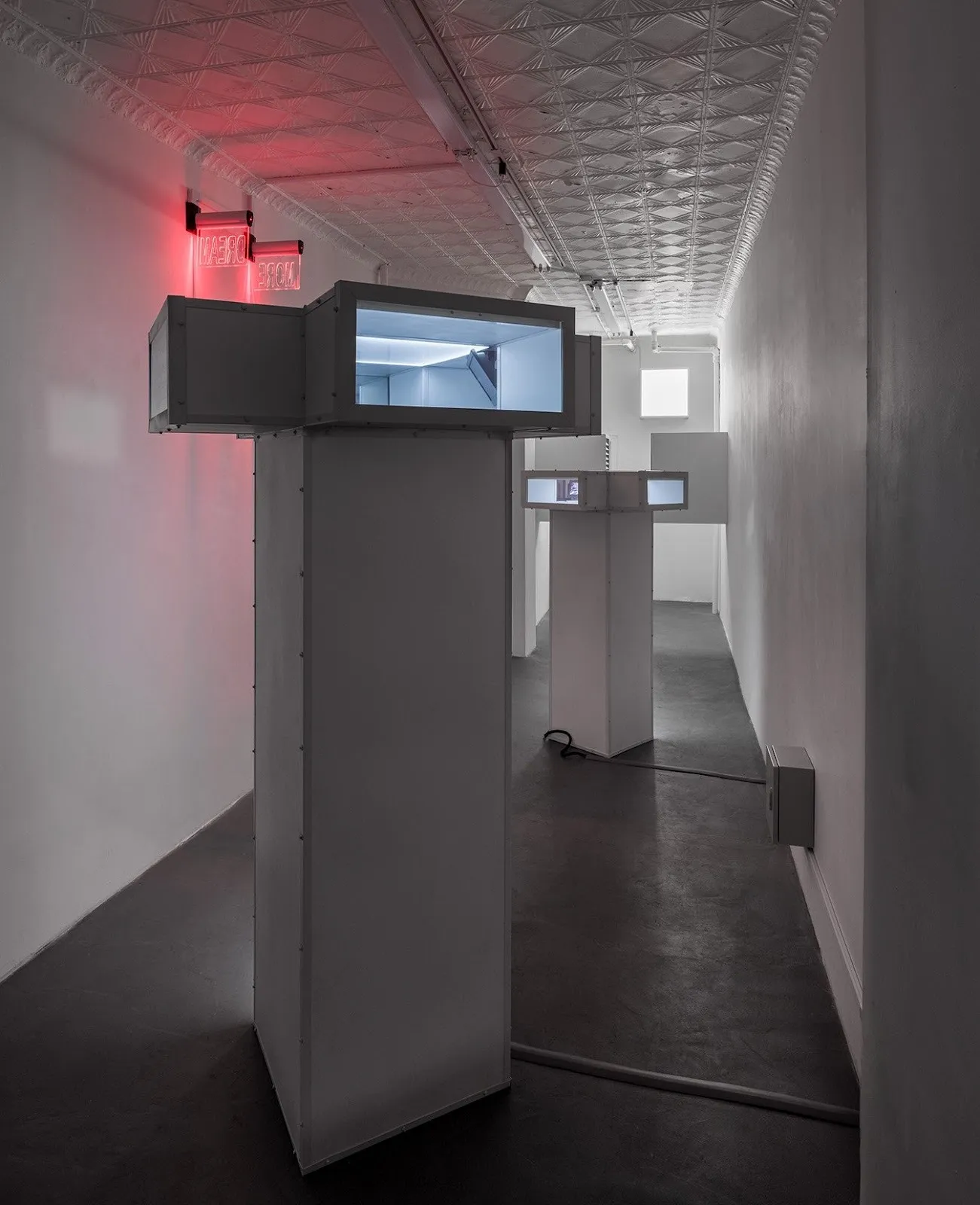 Tall, white sculptural towers with screen-like windows and visible wiring in a dimly lit hallway.