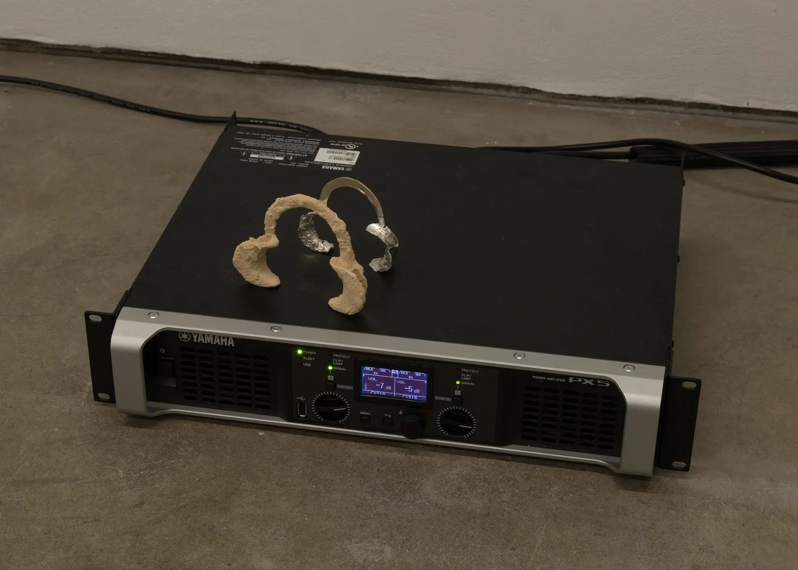 A squat, rectangular Yamaha sound devices sits on the floor. One silvery and one pale wooden mouth retractor are placed on top of the device.