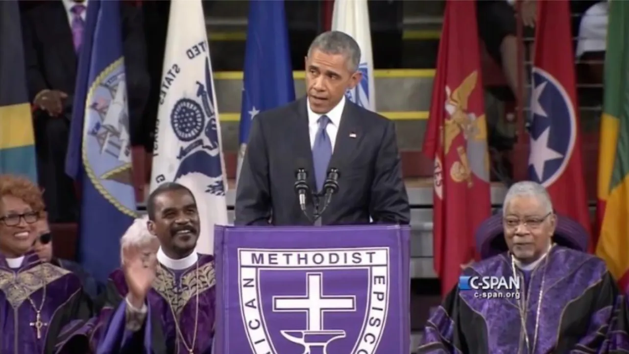 President Barack Obama speaks at a podium during a church service, flanked by clergymen in purple robes and flags in the background.
