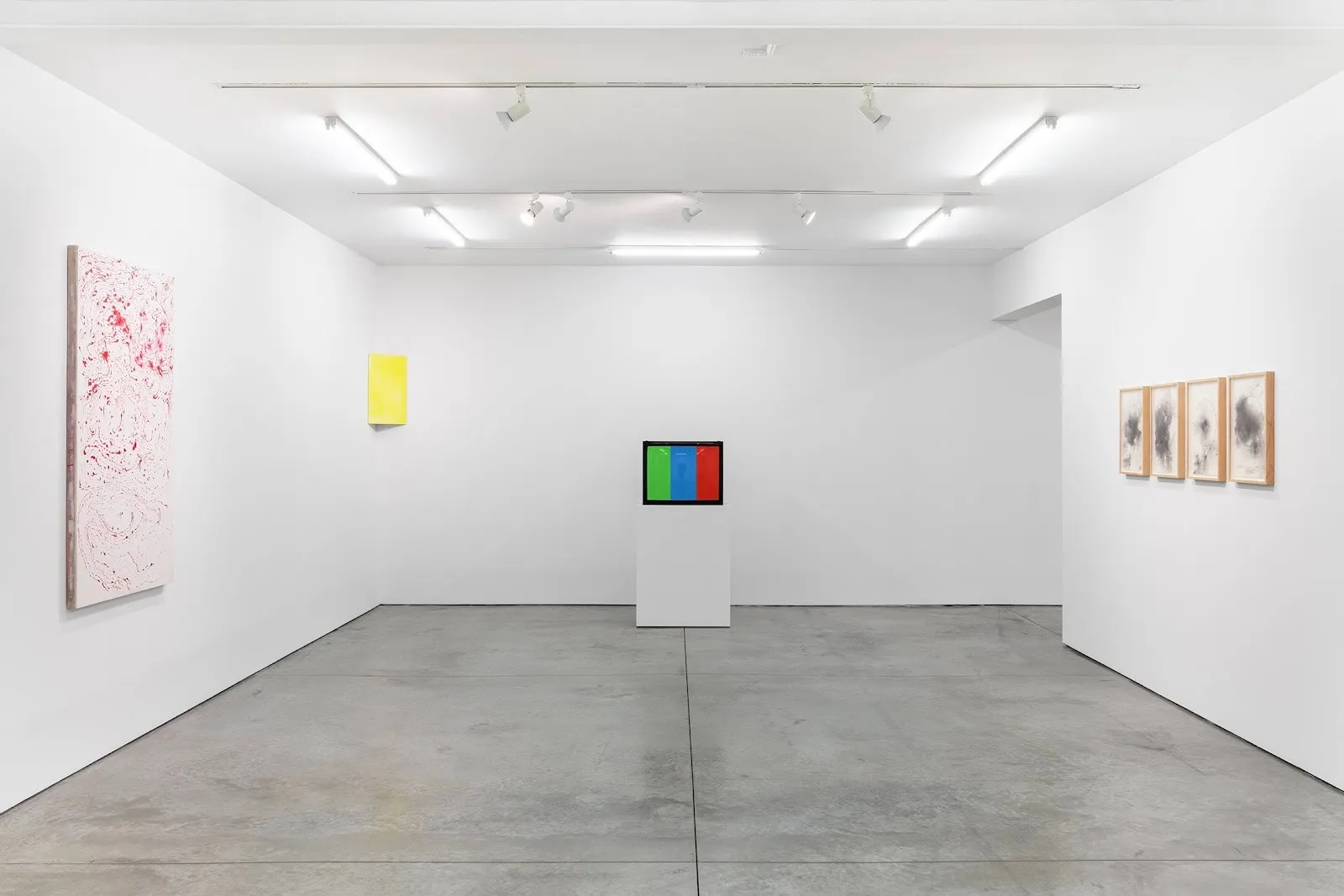 The interior of a modern gallery showcasing abstract artworks. A pink marbled painting is displayed on the left, and a color-blocked sculpture sits on a pedestal in the center, flanked by framed black-and-white drawings on the right.