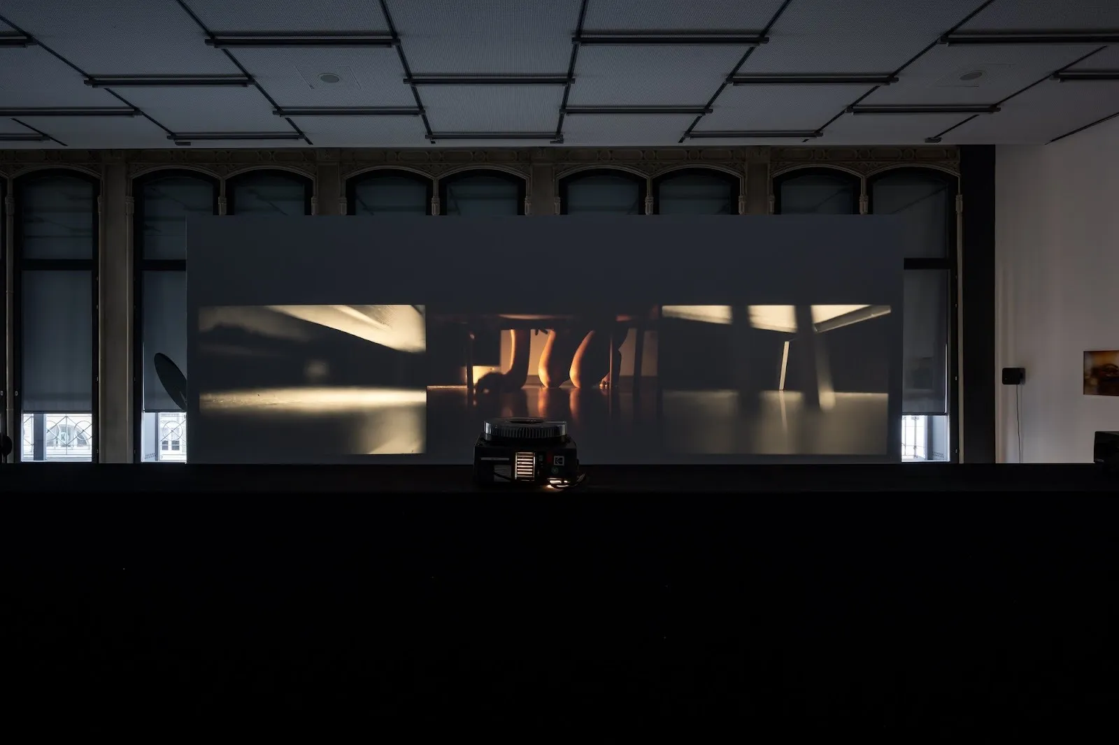 A darkened room with a three-channel projection showing close-up, atmospheric scenes, with a slide projector positioned in front of the screen.