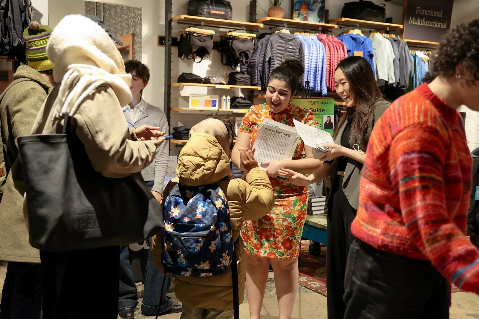 In a clothing store amongst people, two women smile and talk to a child who waves that them.