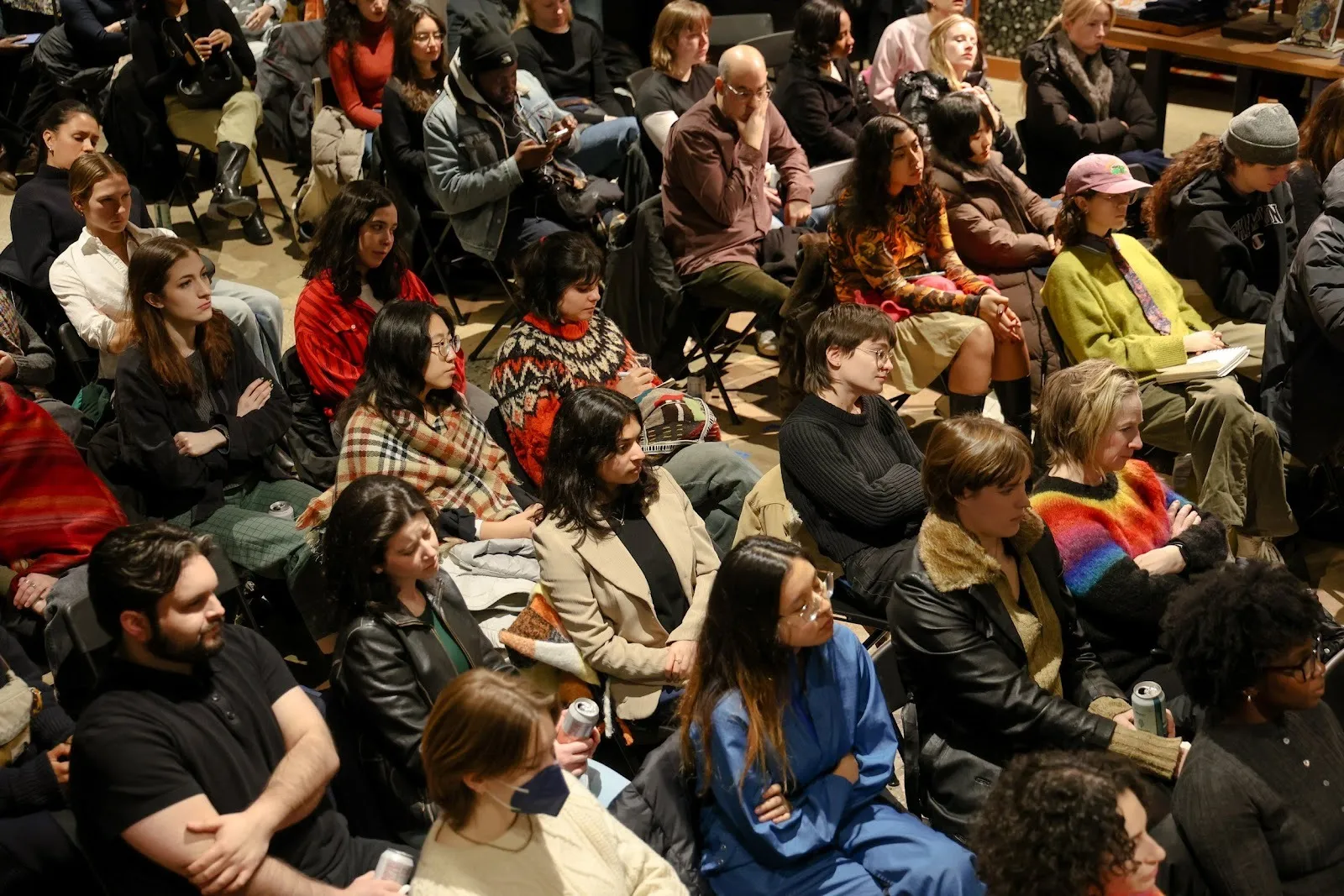 Many people sit in rows of chairs, listening.