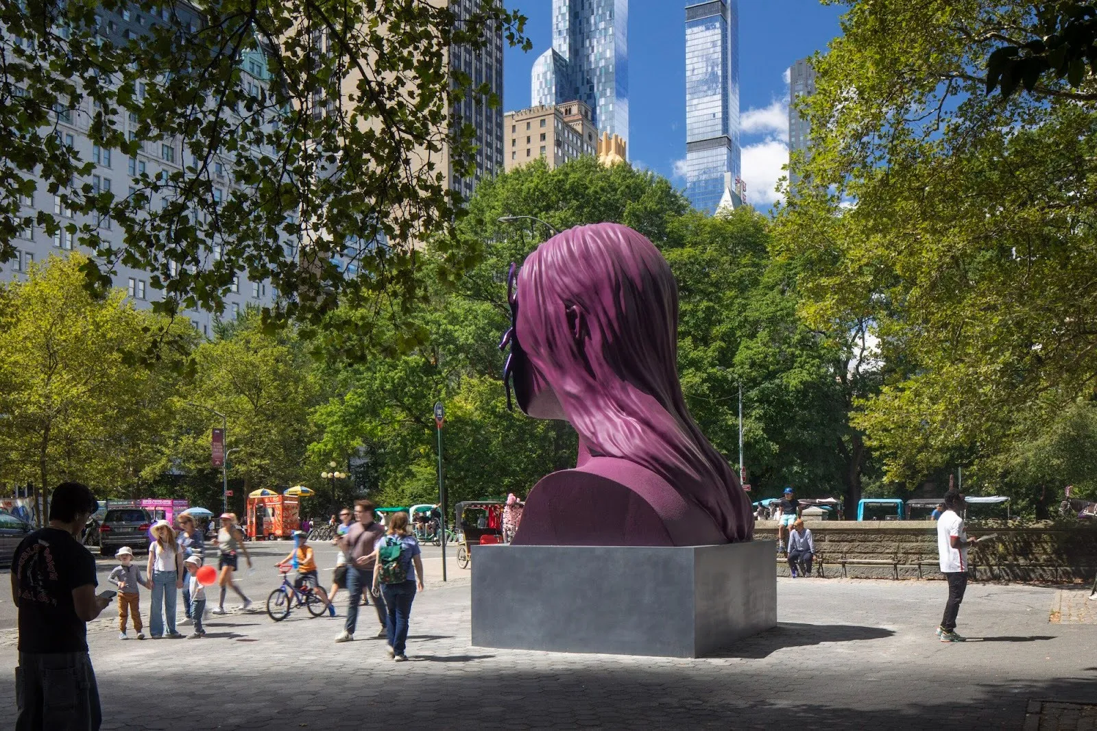 Rear three-quarter view of the magenta bust sculpture with flowing hair and the beetle-shaped faceplate, set against trees and tall city buildings in the background.