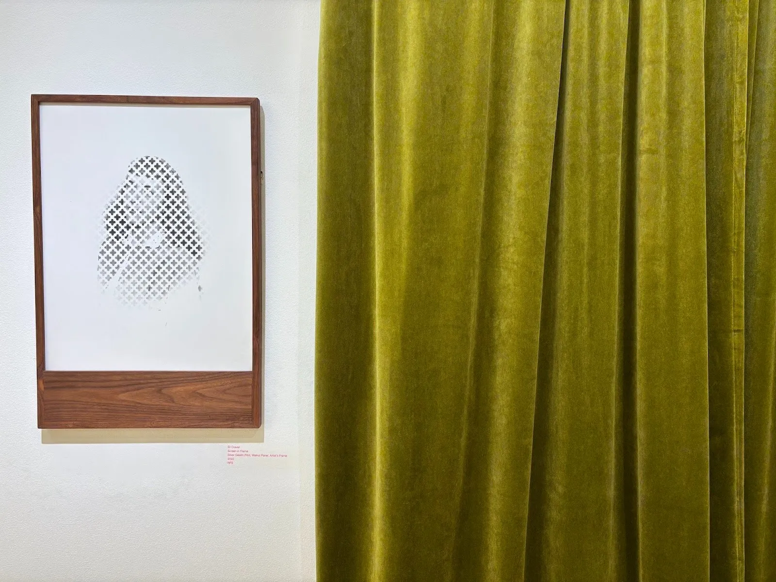Framed artwork of a partially obscured portrait made from a cut-out grid, next to green velvet curtains.