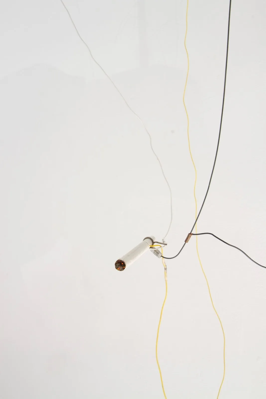 A simple sculpture made from clear, yellow, and black wires join and support a single lit cigarette hanging mid-air.
