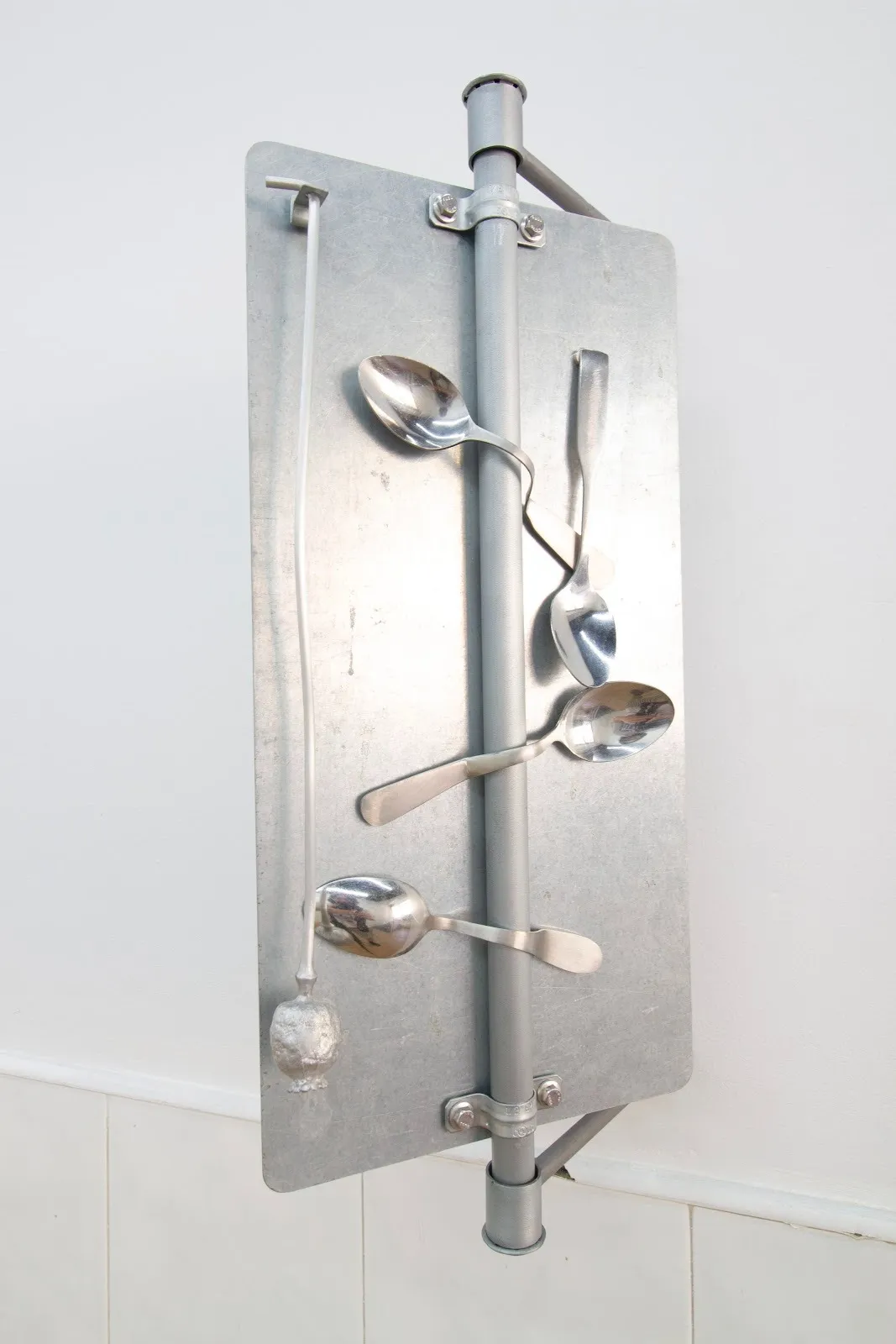 A street sign-like sculpture has a metal backing with three spoons bent around the supporting pole.